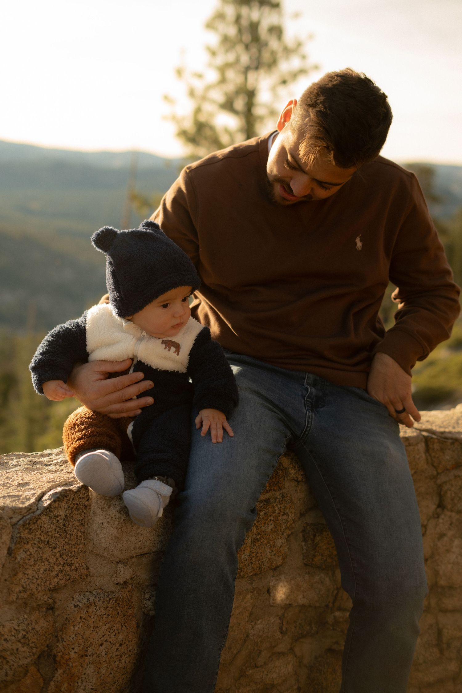 Family enjoying golden hour views from a scenic mountain overlook with stone wall barrier.
