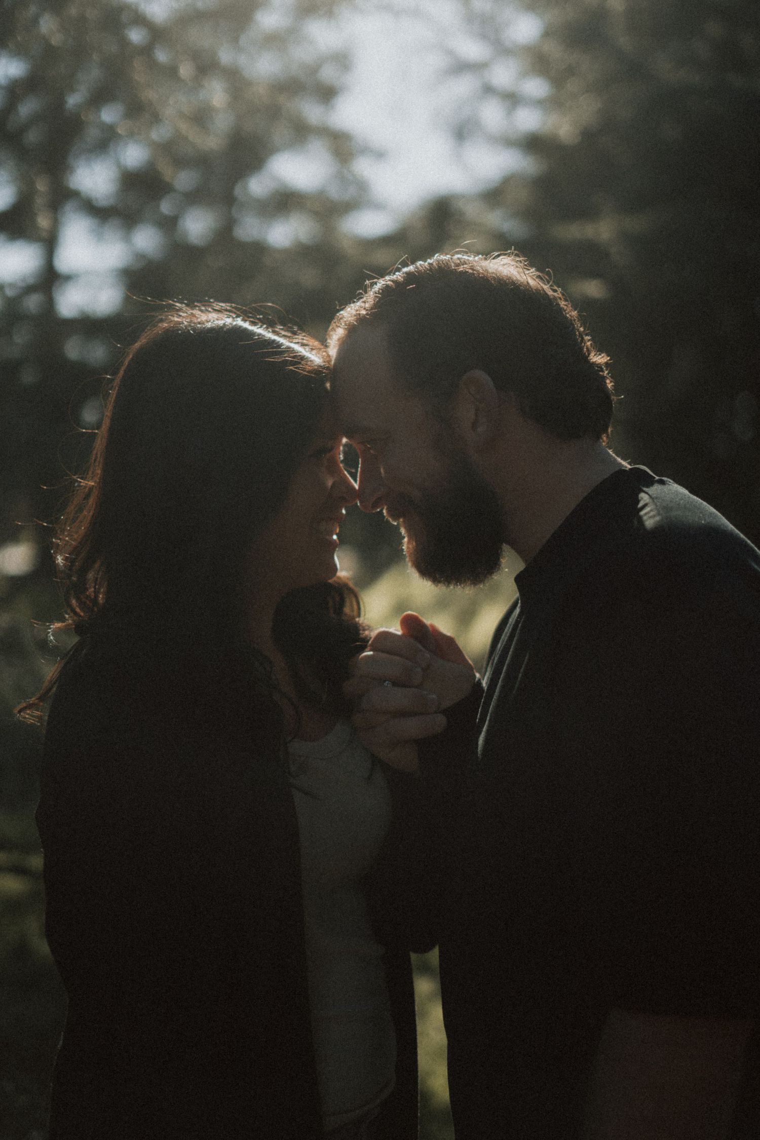 Backlit couple in a romantic embrace against a forested background.