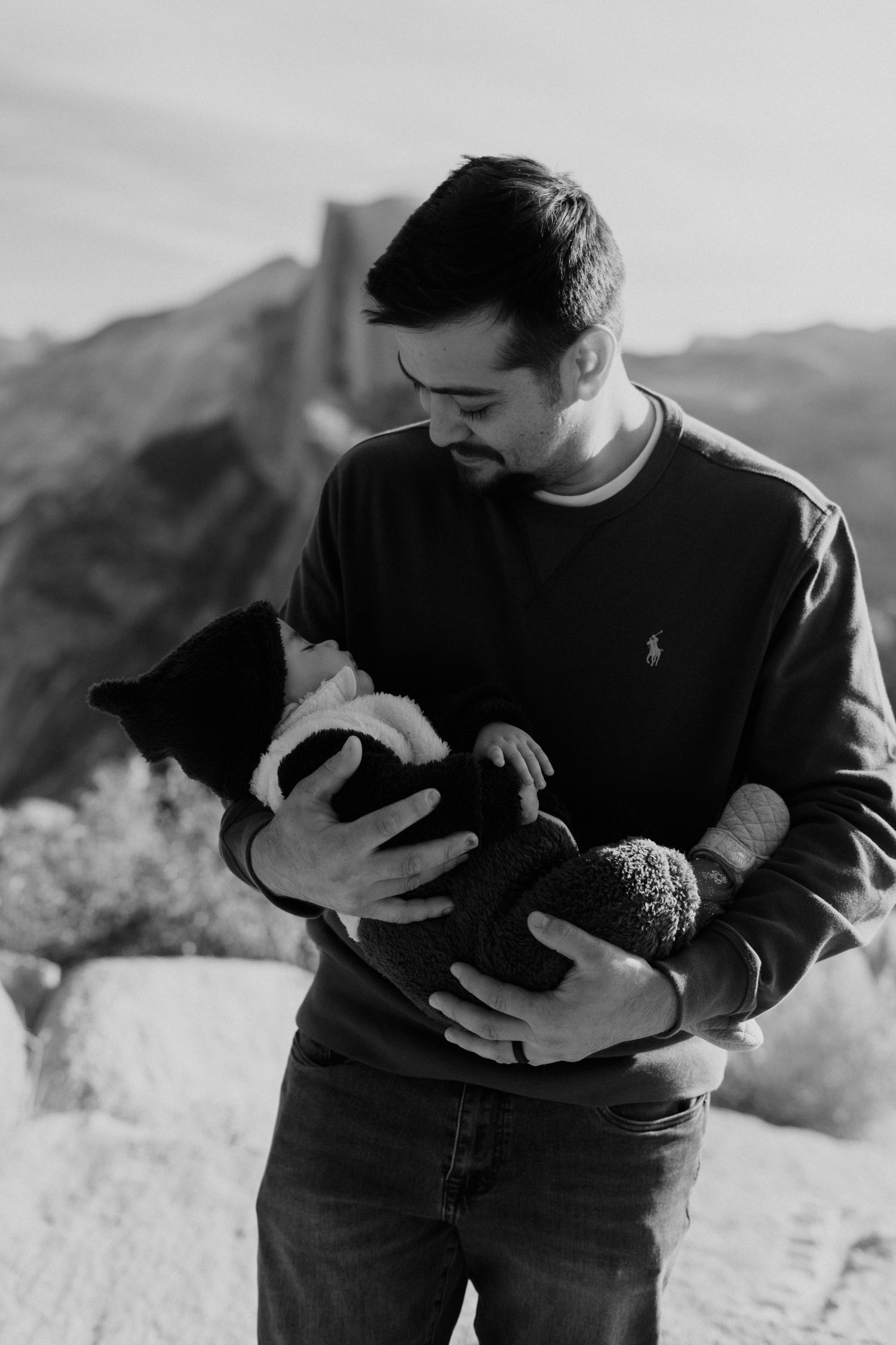 Black and white portrait of tender parenting moment against mountain landscape.