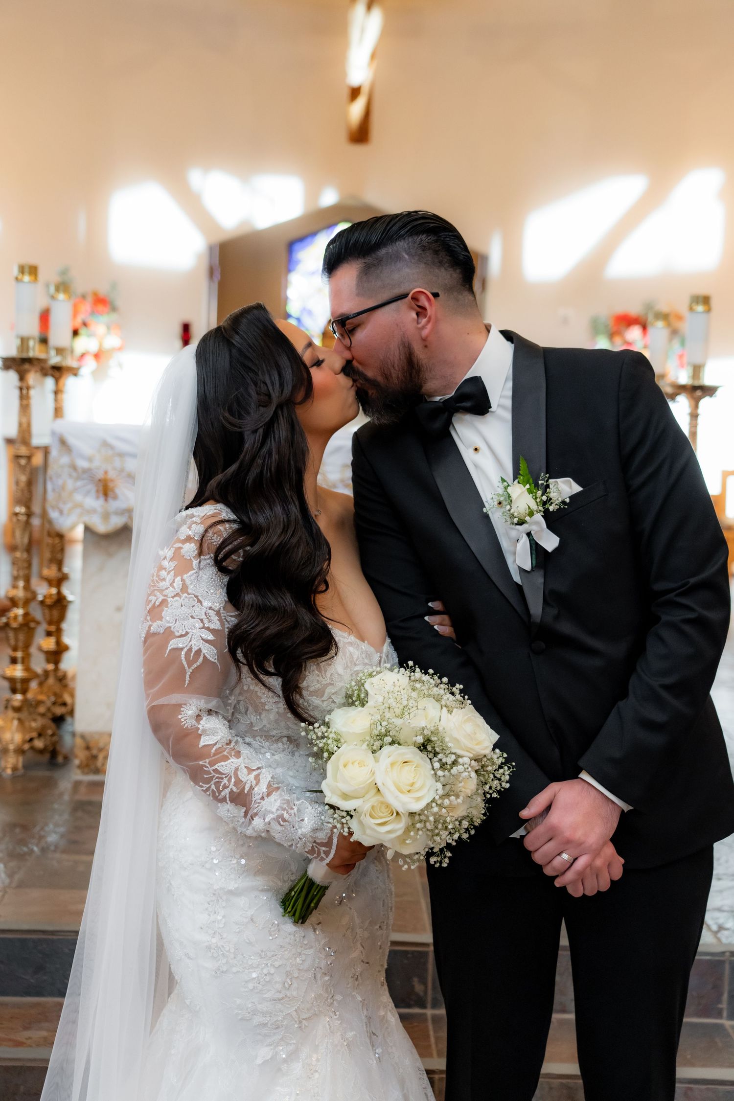 Wedding couple sharing intimate kisses while holding a white floral bouquet in a church.