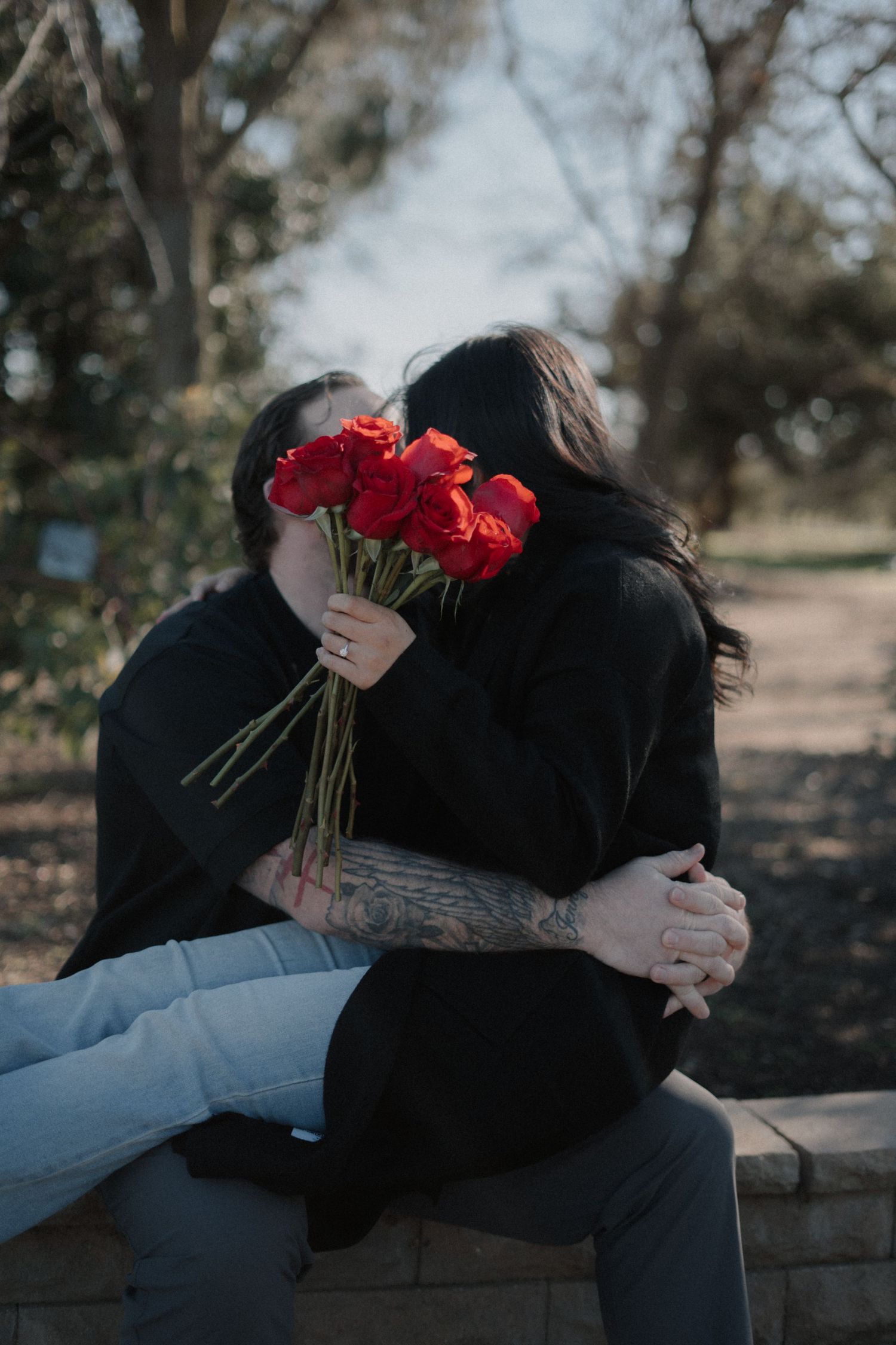 Couple sharing a tender moment on stone steps with red roses.