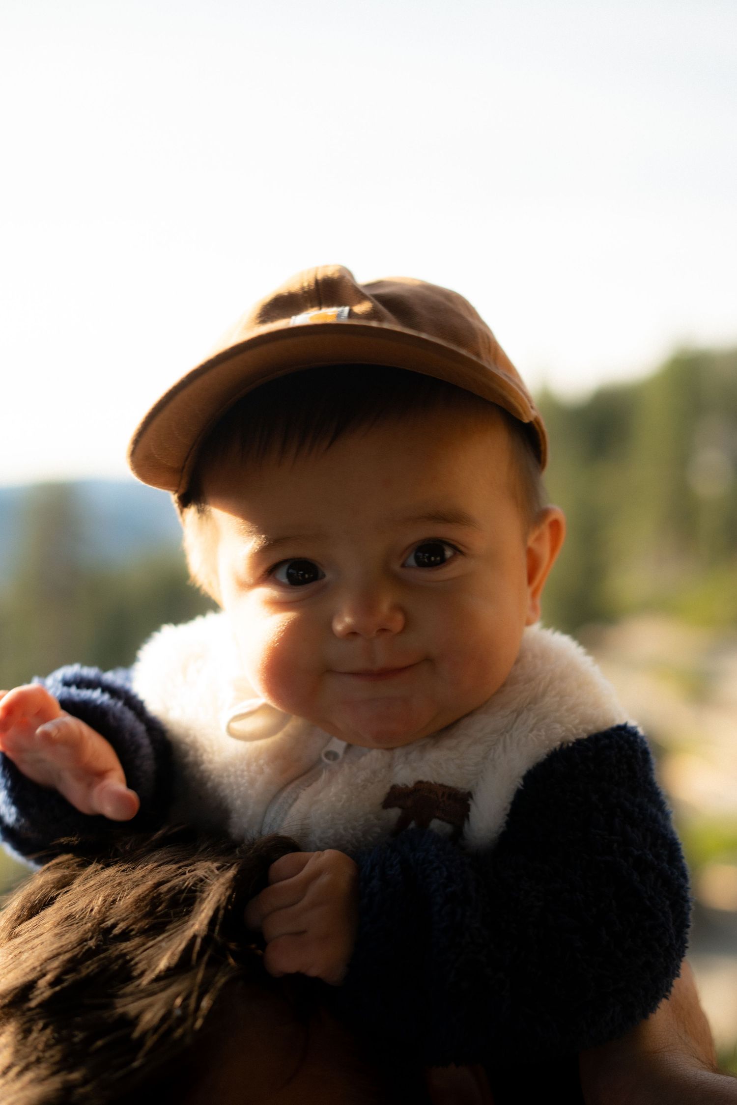Close-up portrait of baby in baseball cap and navy fleece jacket.