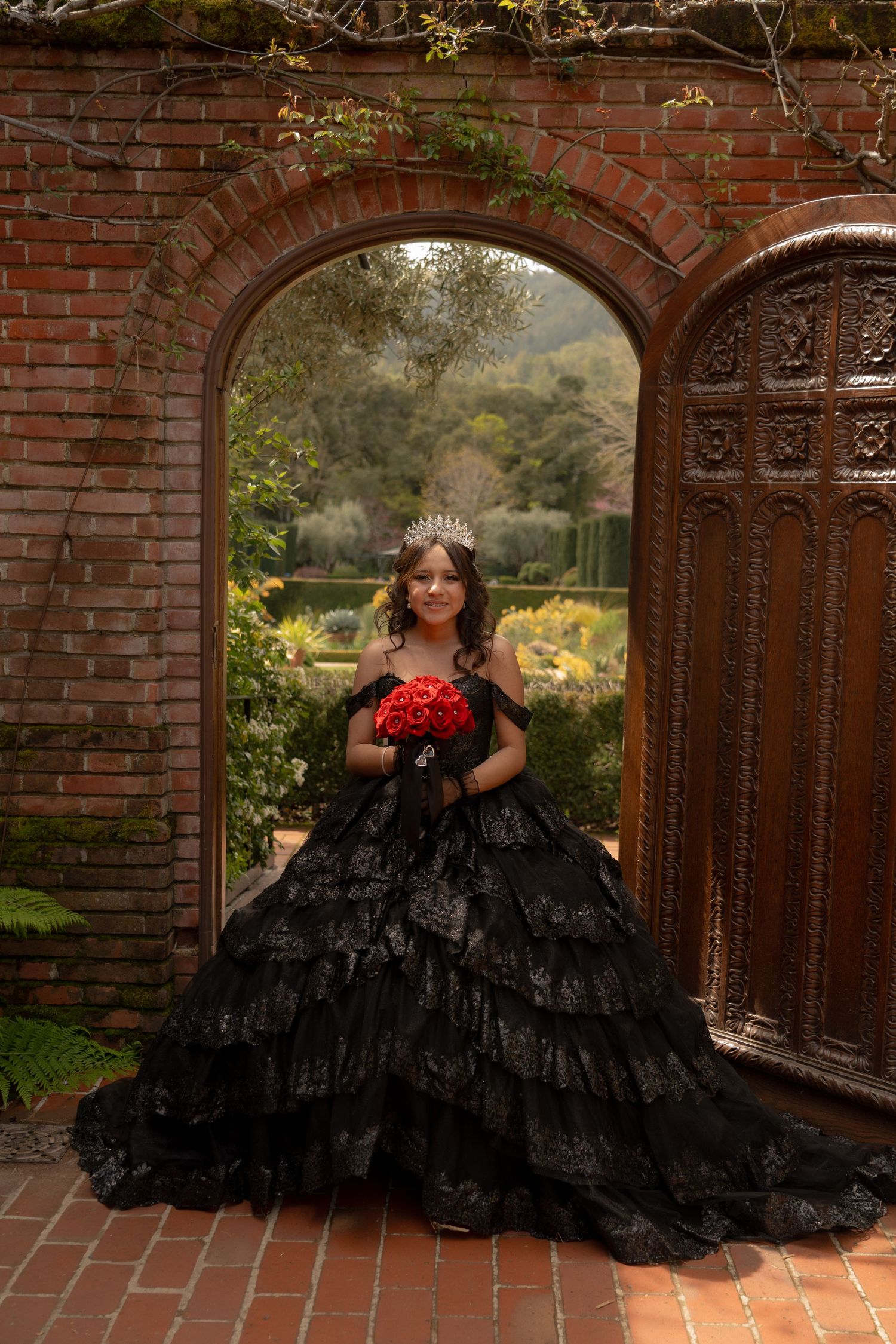 Dramatic portrait of person in black ball gown posing against brick archway.