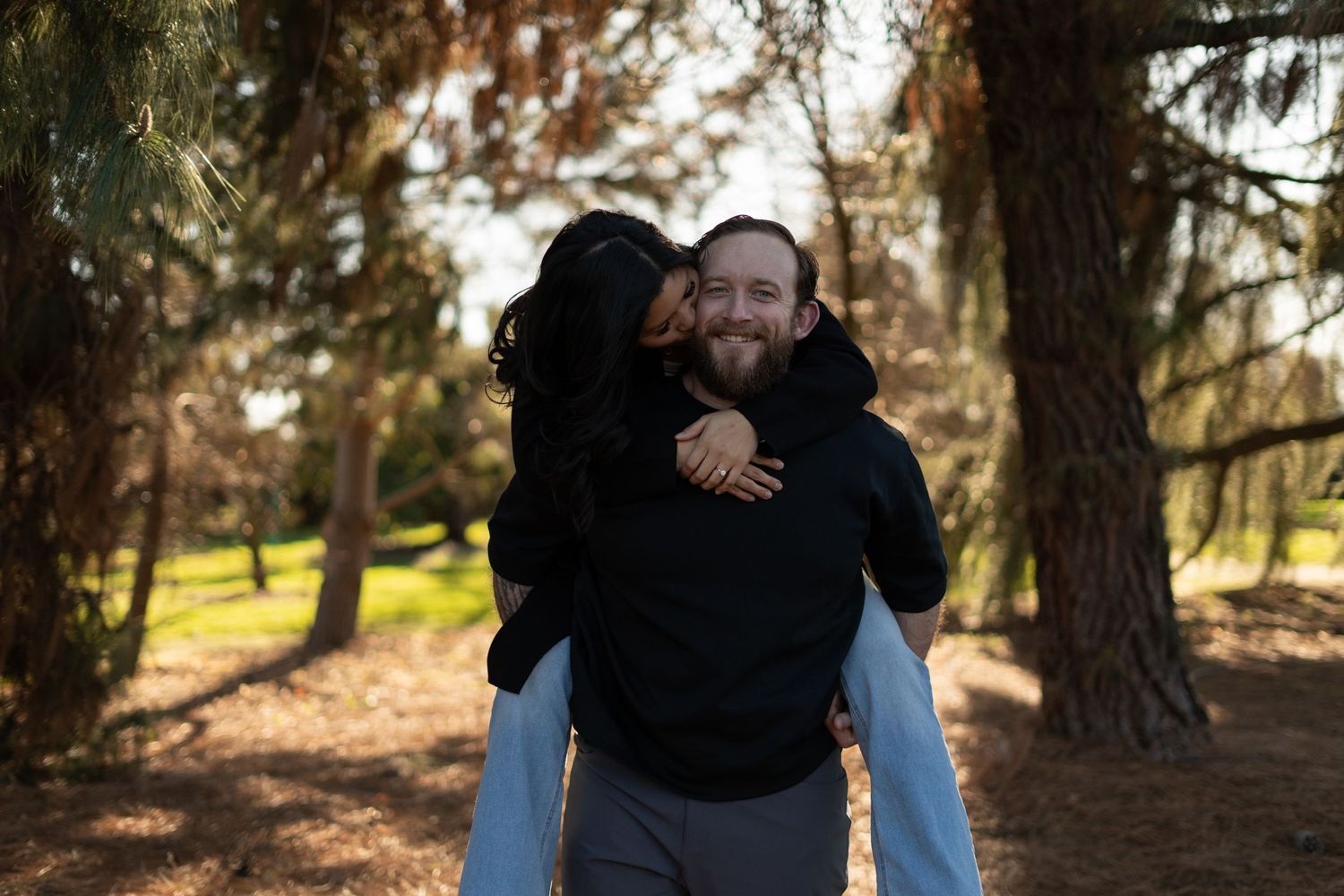 Joyful piggyback ride moment captured in a sunlit forest setting.