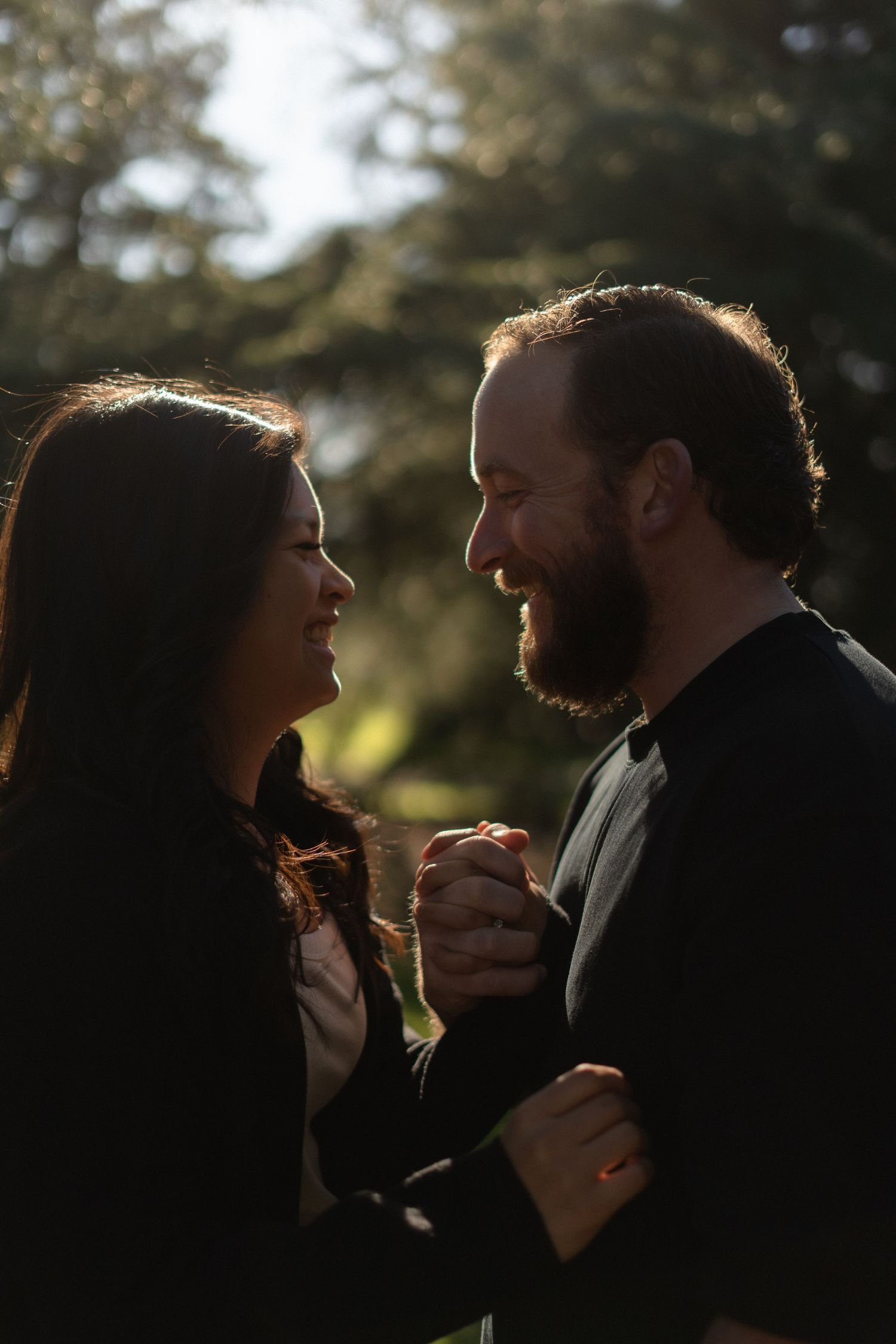 A romantic couple sharing an intimate moment in a sun-dappled forest setting.