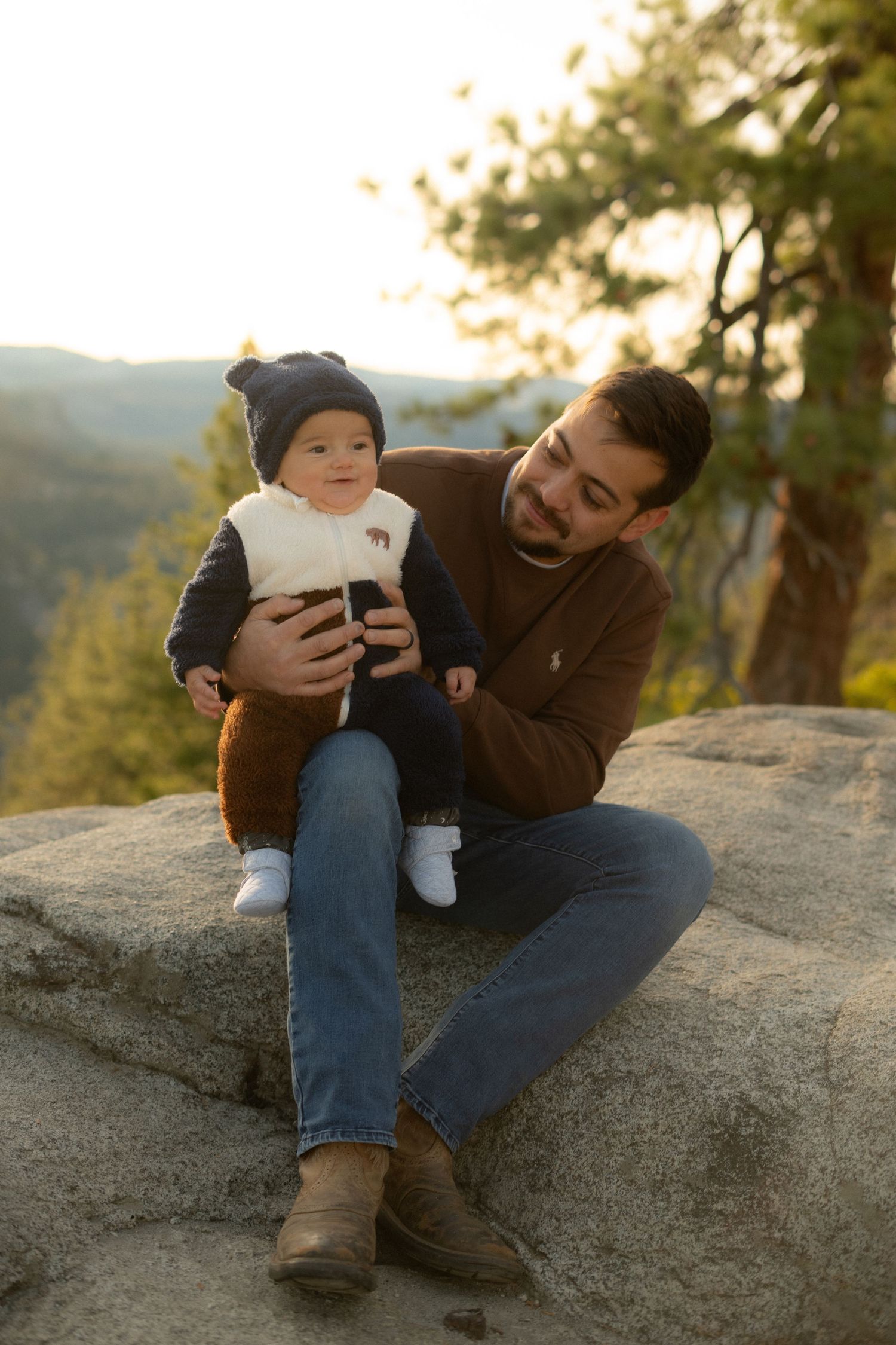 Parent and baby sharing tender moment while sitting on rocky outcrop in nature.