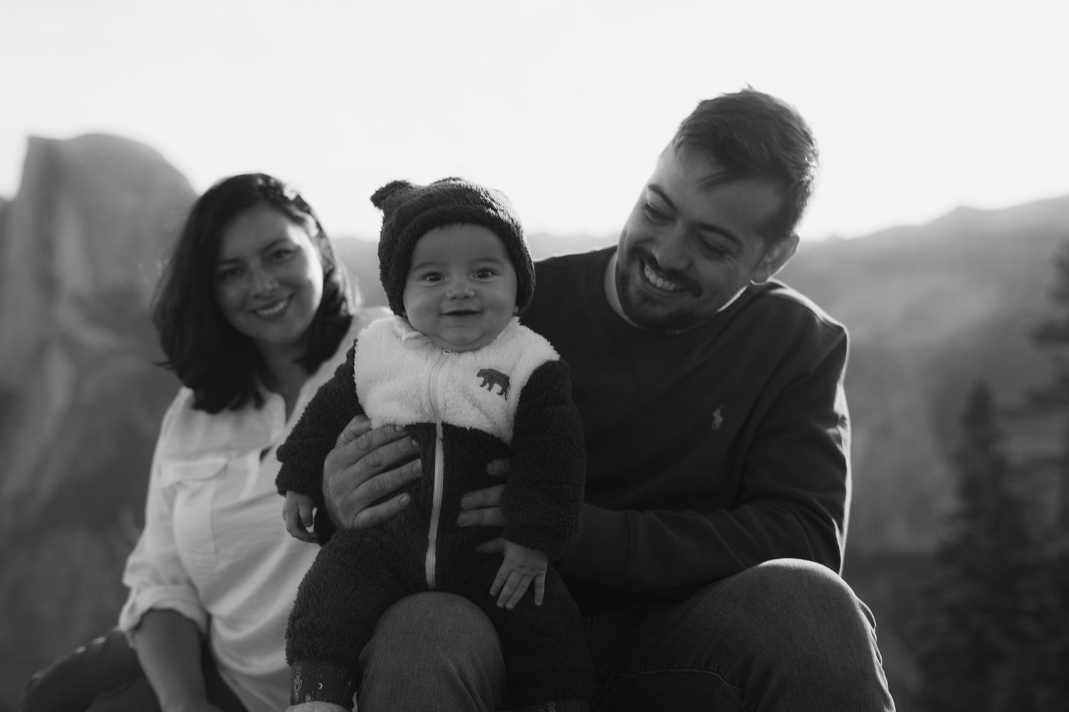 Black and white portrait of family sharing tender moment against mountain landscape.
