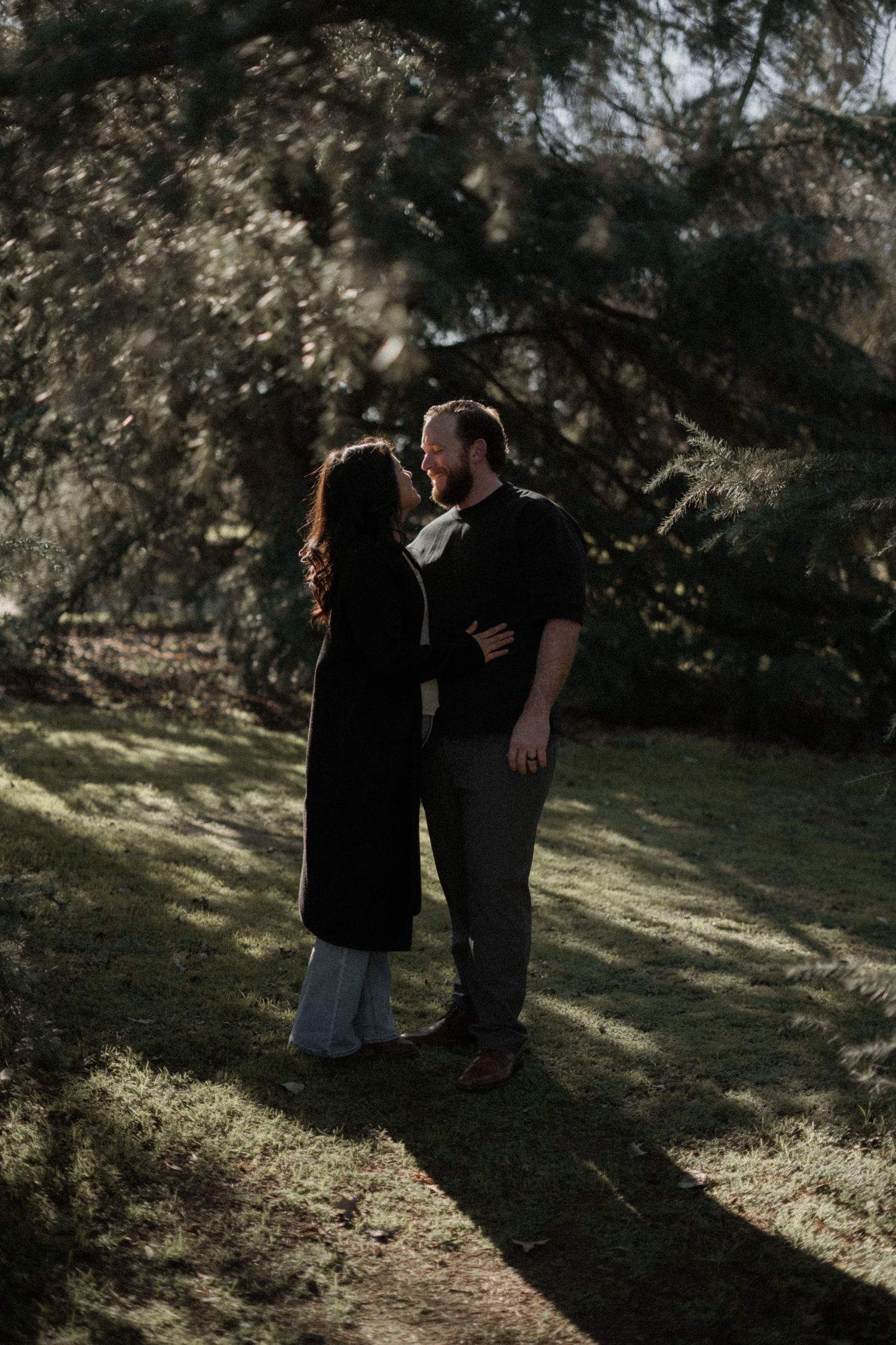 A couple sharing an intimate moment in dappled sunlight under trees.