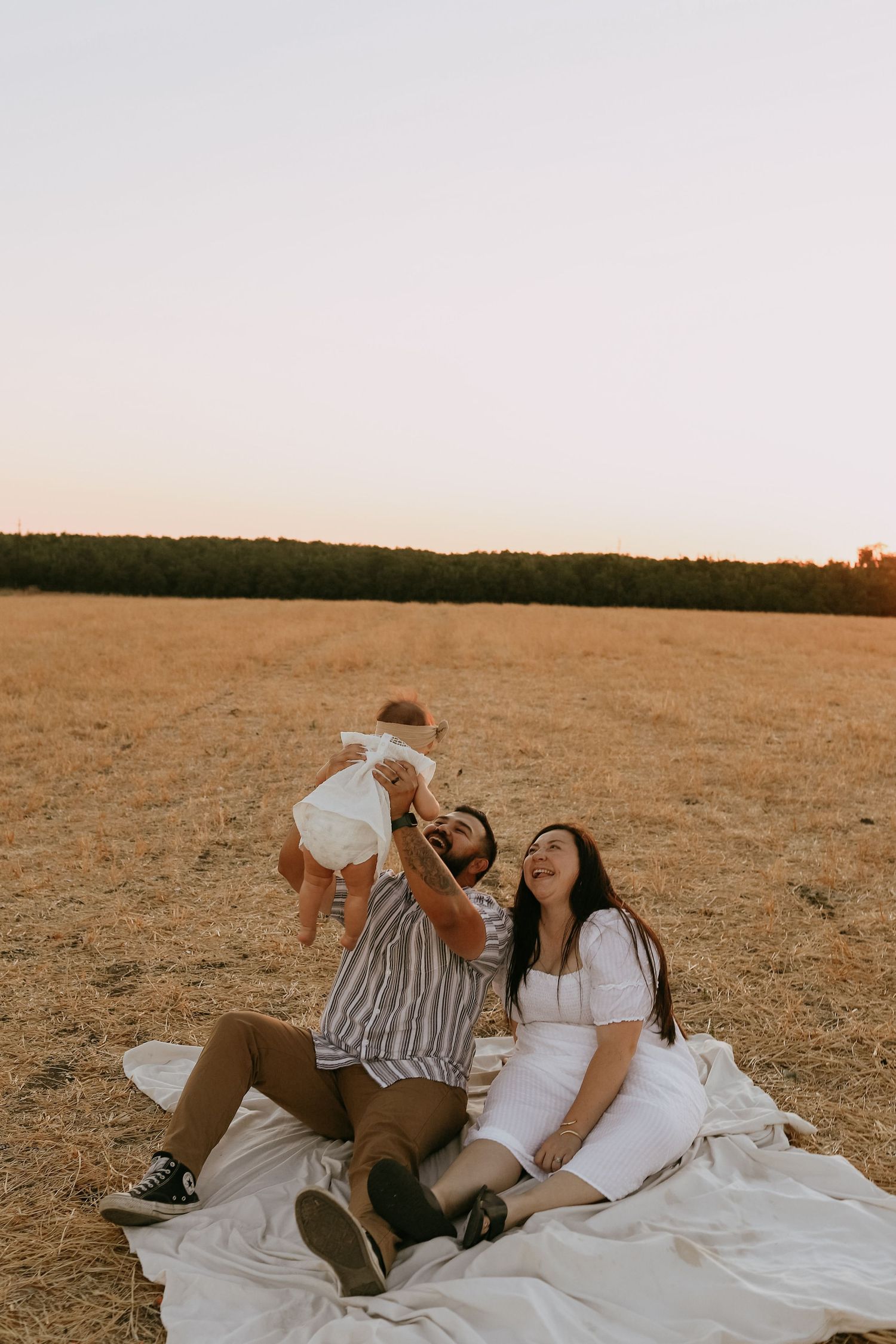 A relaxed family moment on a white blanket in a golden field at sunset.