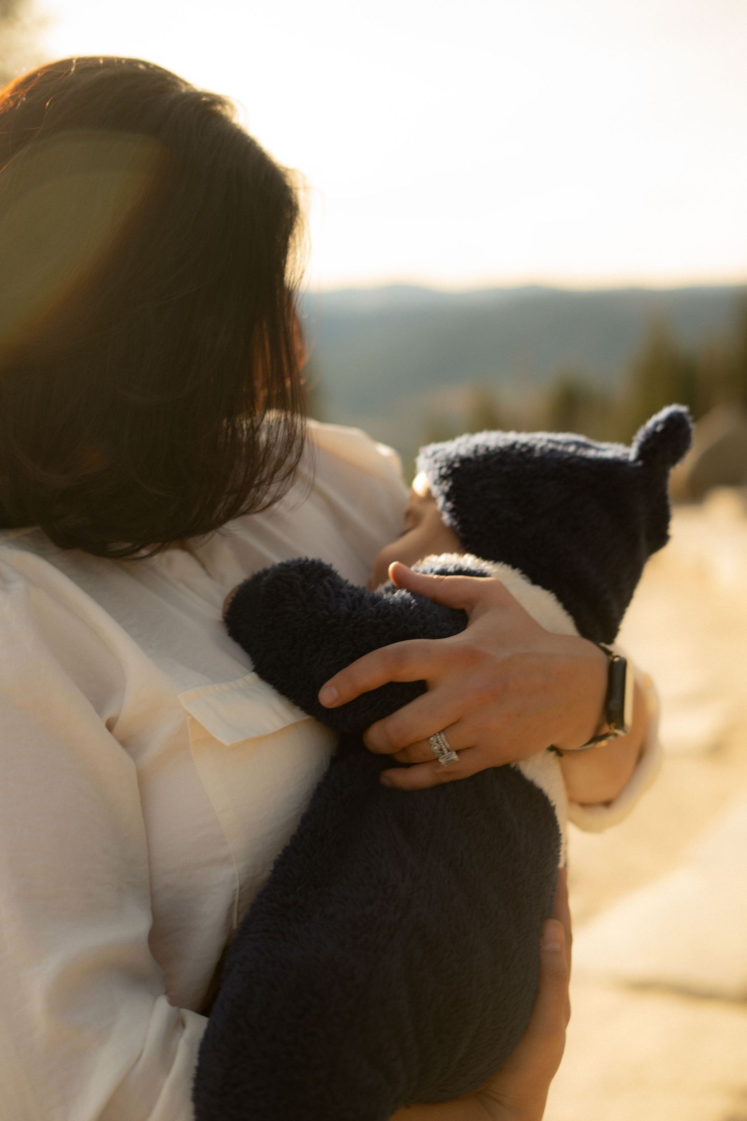 Intimate family embrace captured in soft golden hour lighting at mountain viewpoint.