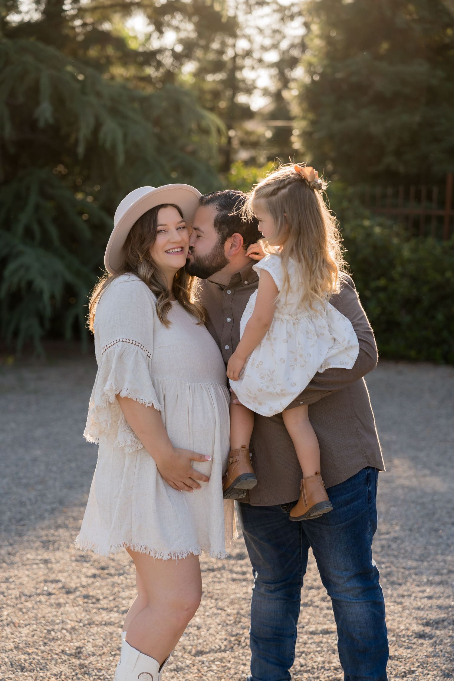 A romantic sunset photoshoot shows a family sharing tender moments together on a gravel path at golden hour.