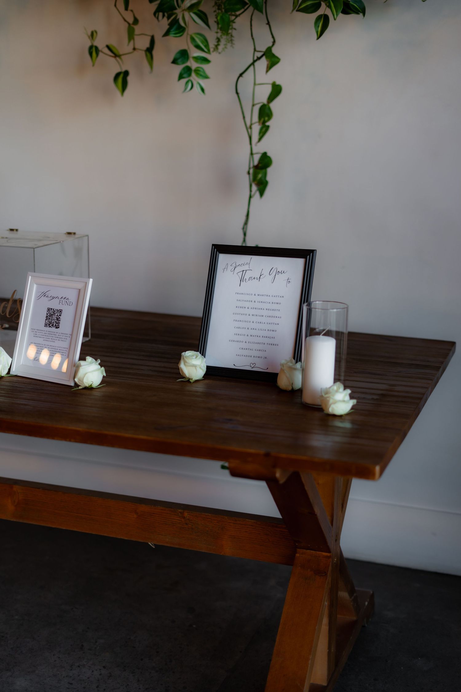 Rustic wooden table decorated with white roses and frames for wedding reception.