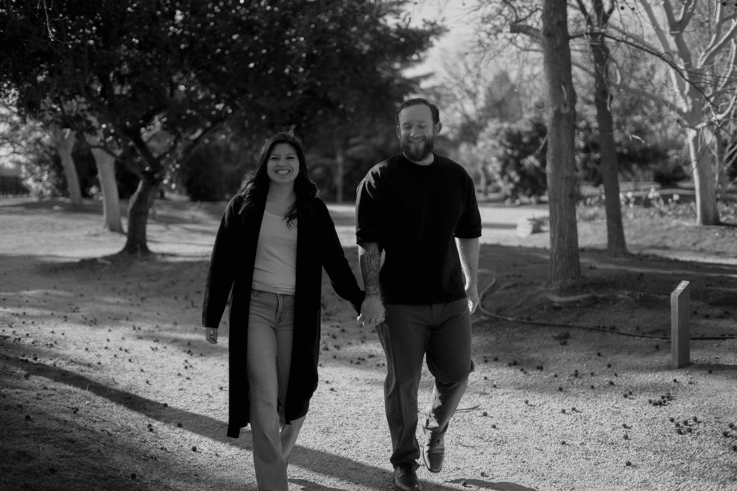 Black and white photo of a couple strolling through a tree-lined path.