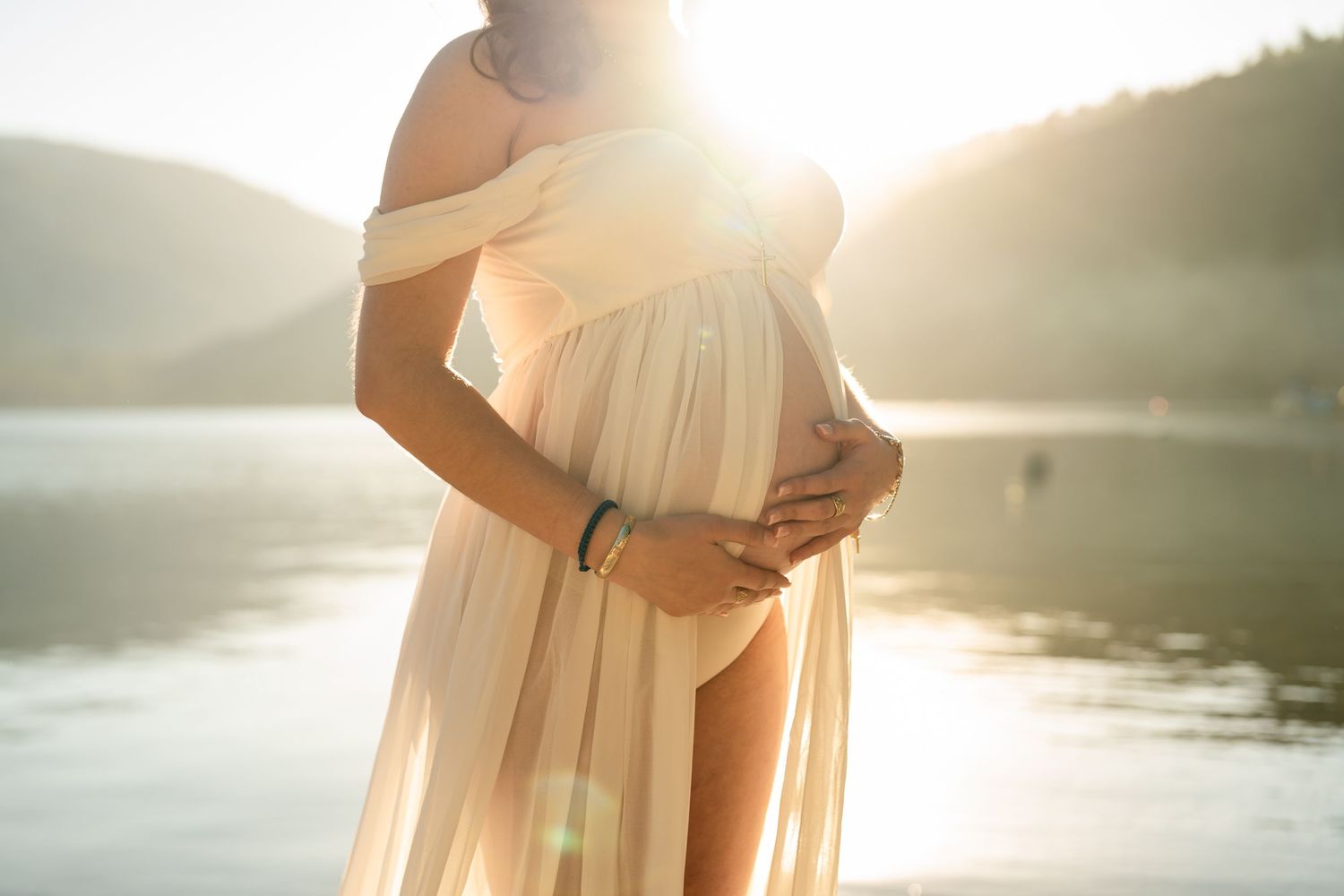 A person in a flowy white dress stands by a serene lake at sunset creating a dreamy silhouette.