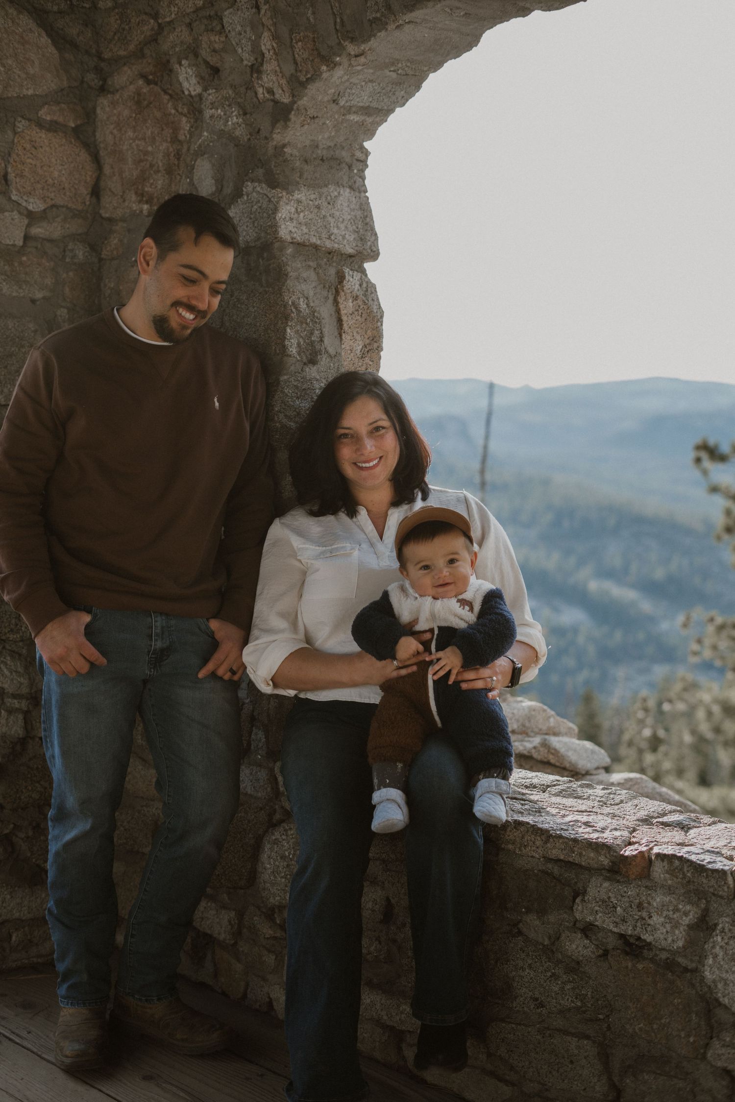 Candid family portrait session at mountain overlook with rustic stone wall.