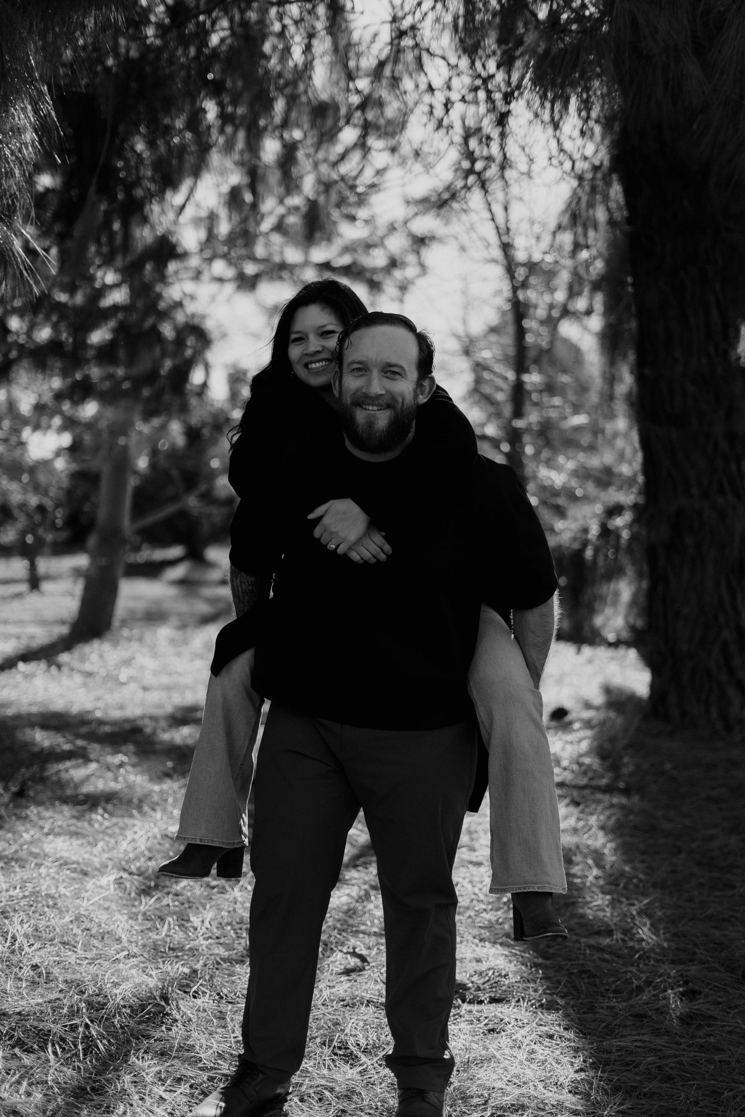 Black and white portrait of a happy couple enjoying a piggyback ride in nature.