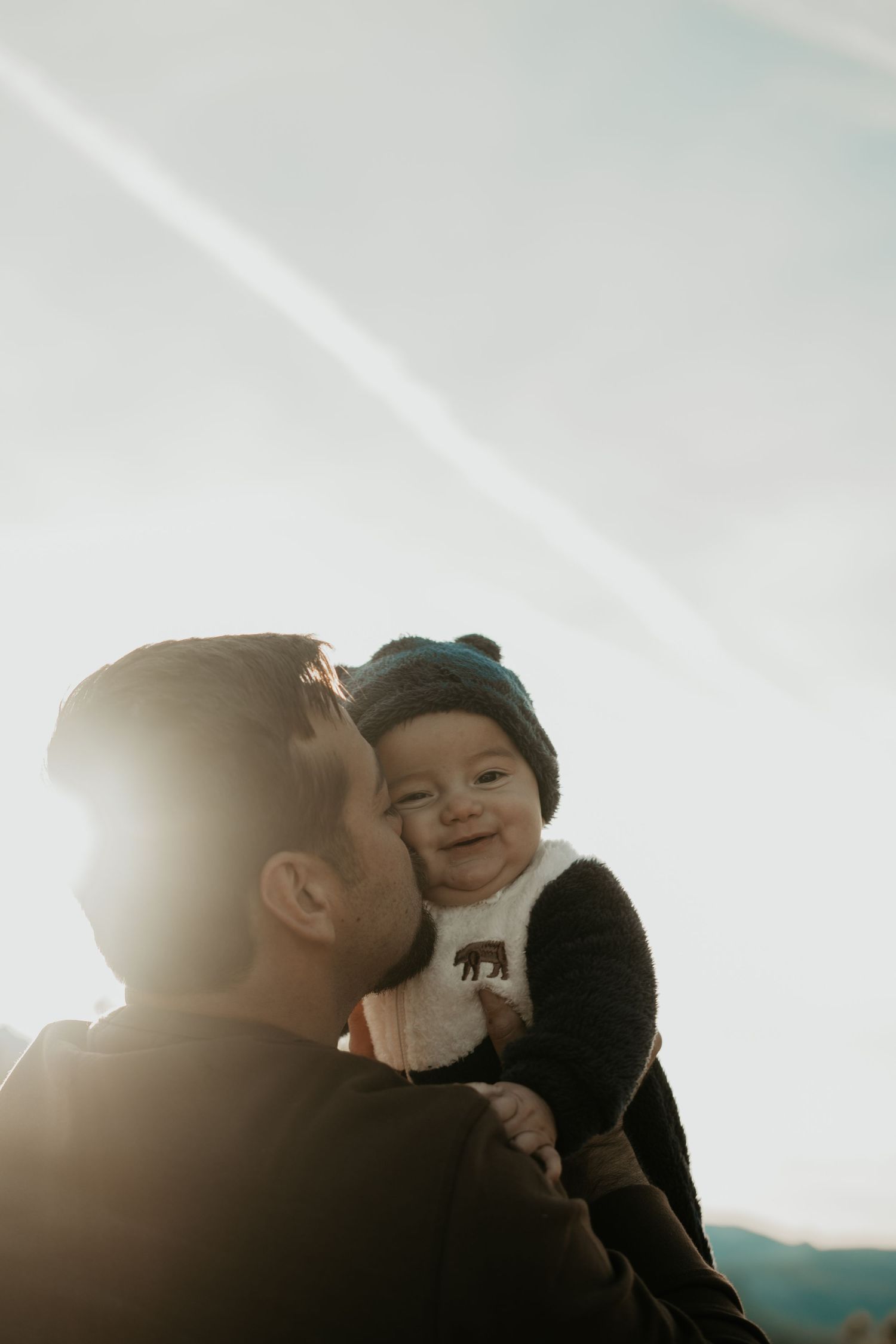 Backlit portrait of parent and baby sharing joyful moment against bright sky.