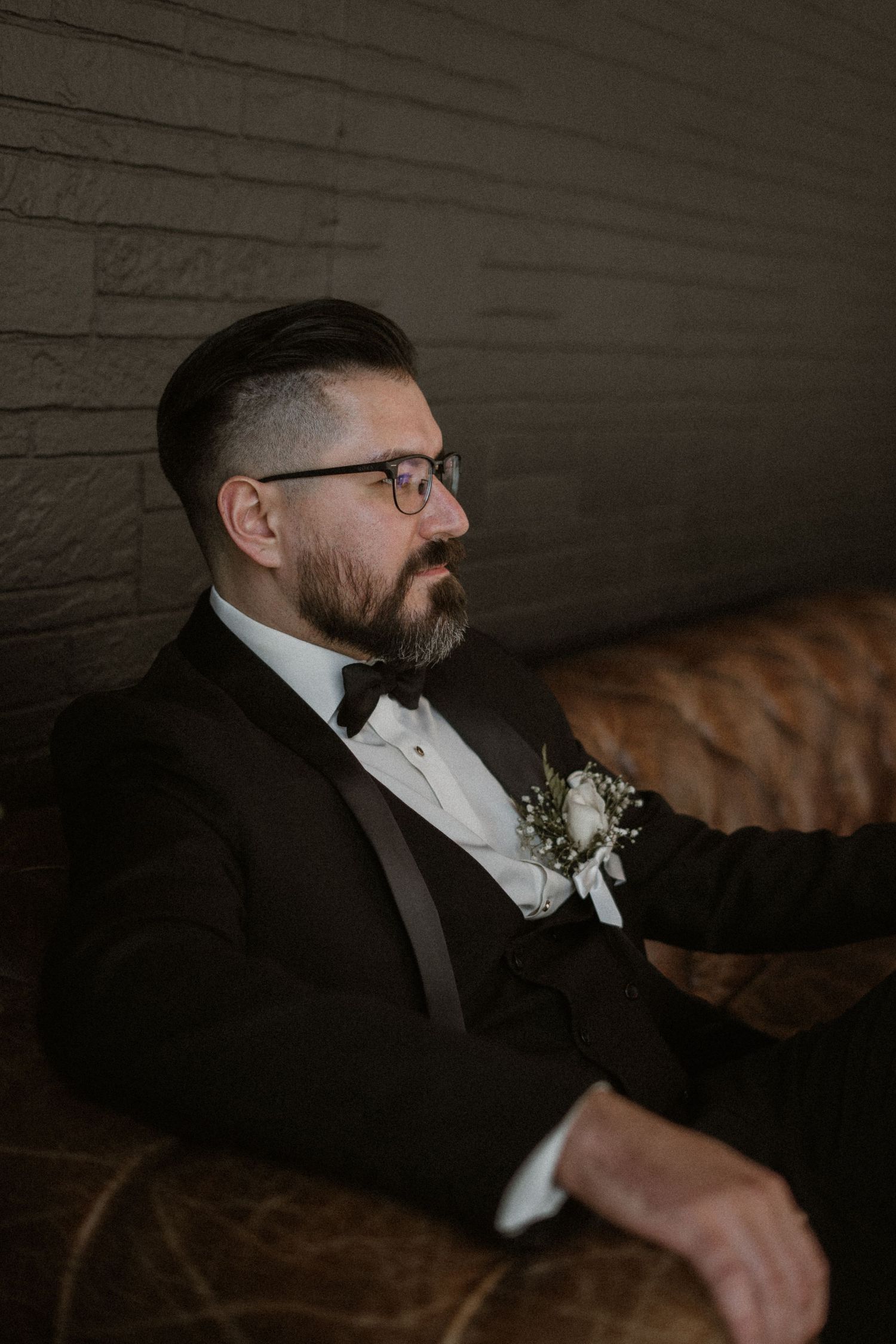Classic formal portrait in black tuxedo seated on leather couch.