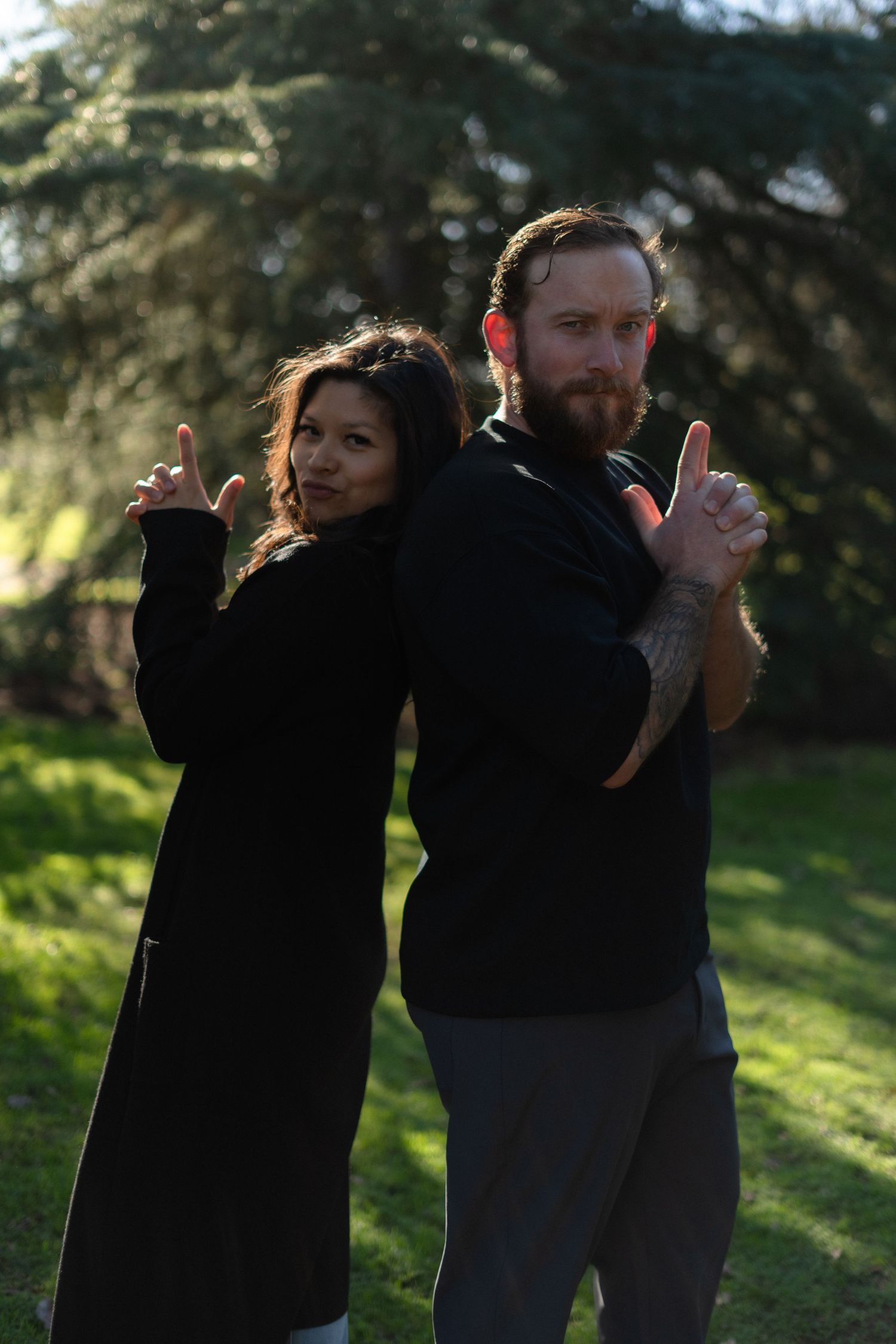 A couple striking Charlie's Angels poses in a sunlit garden.