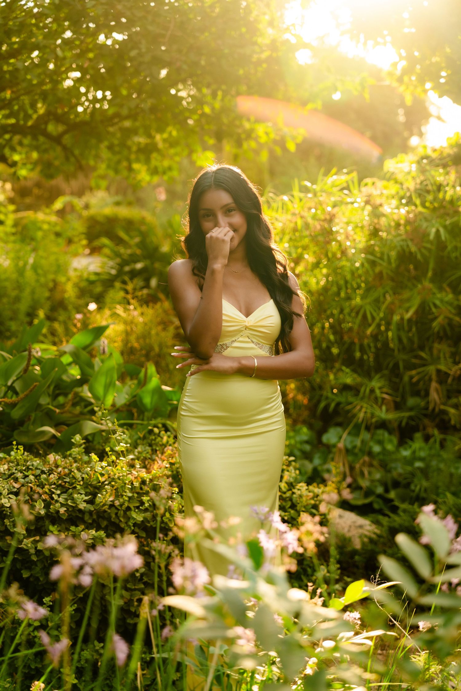 A person in a yellow dress sits among blooming wildflowers in a sunlit garden during golden hour.