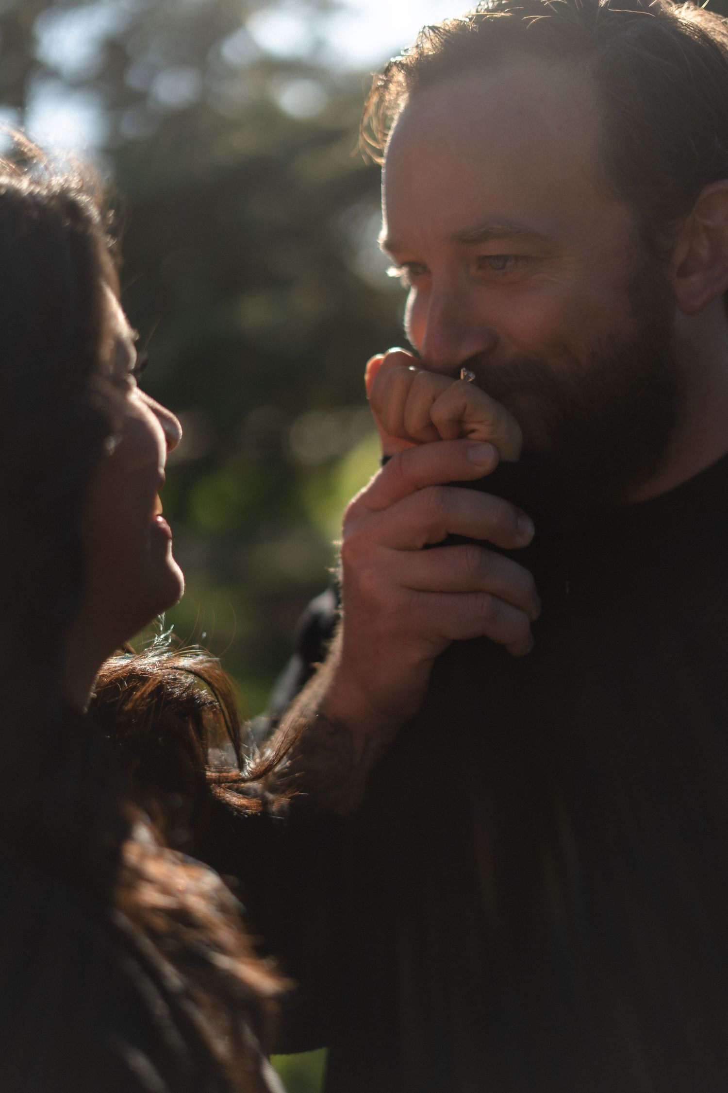 A couple sharing an intimate moment in warm sunlight filtering through trees.