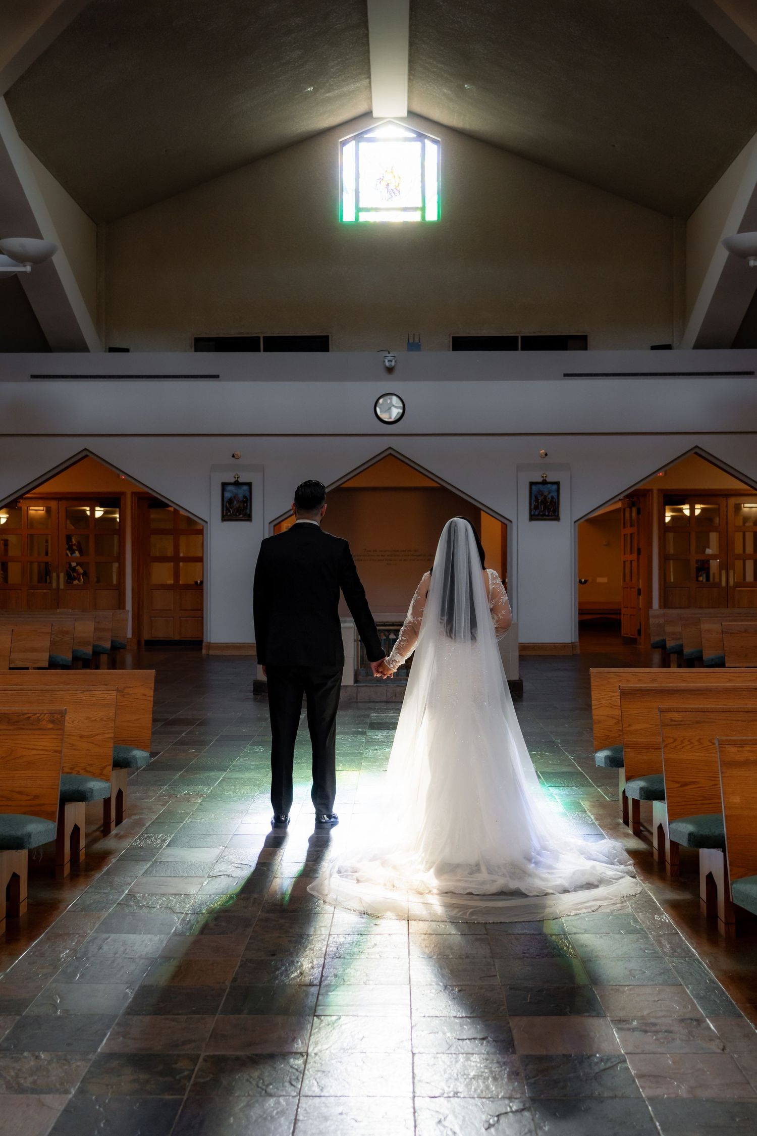 Silhouettes of a bride and groom standing in a church aisle with dramatic lighting.
