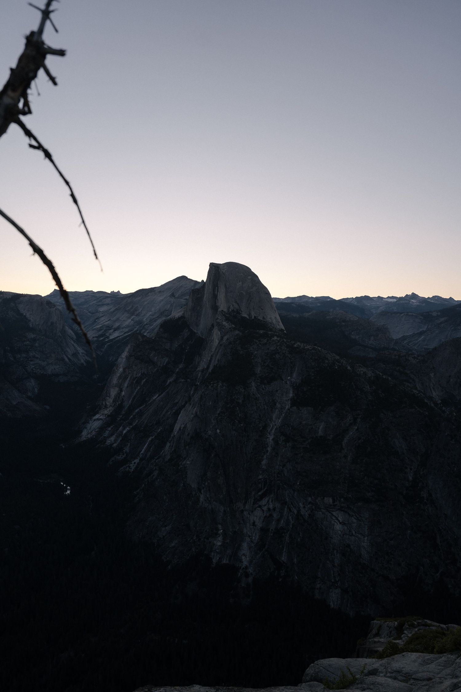 Dark silhouette of Half Dome mountain peak in Yosemite National Park at dusk against fading light in the sky.