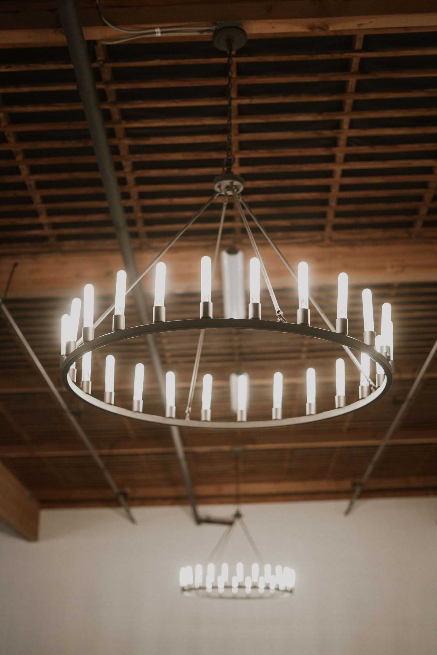 Large circular chandelier with glowing white candle-style lights hanging from a wooden beam ceiling.