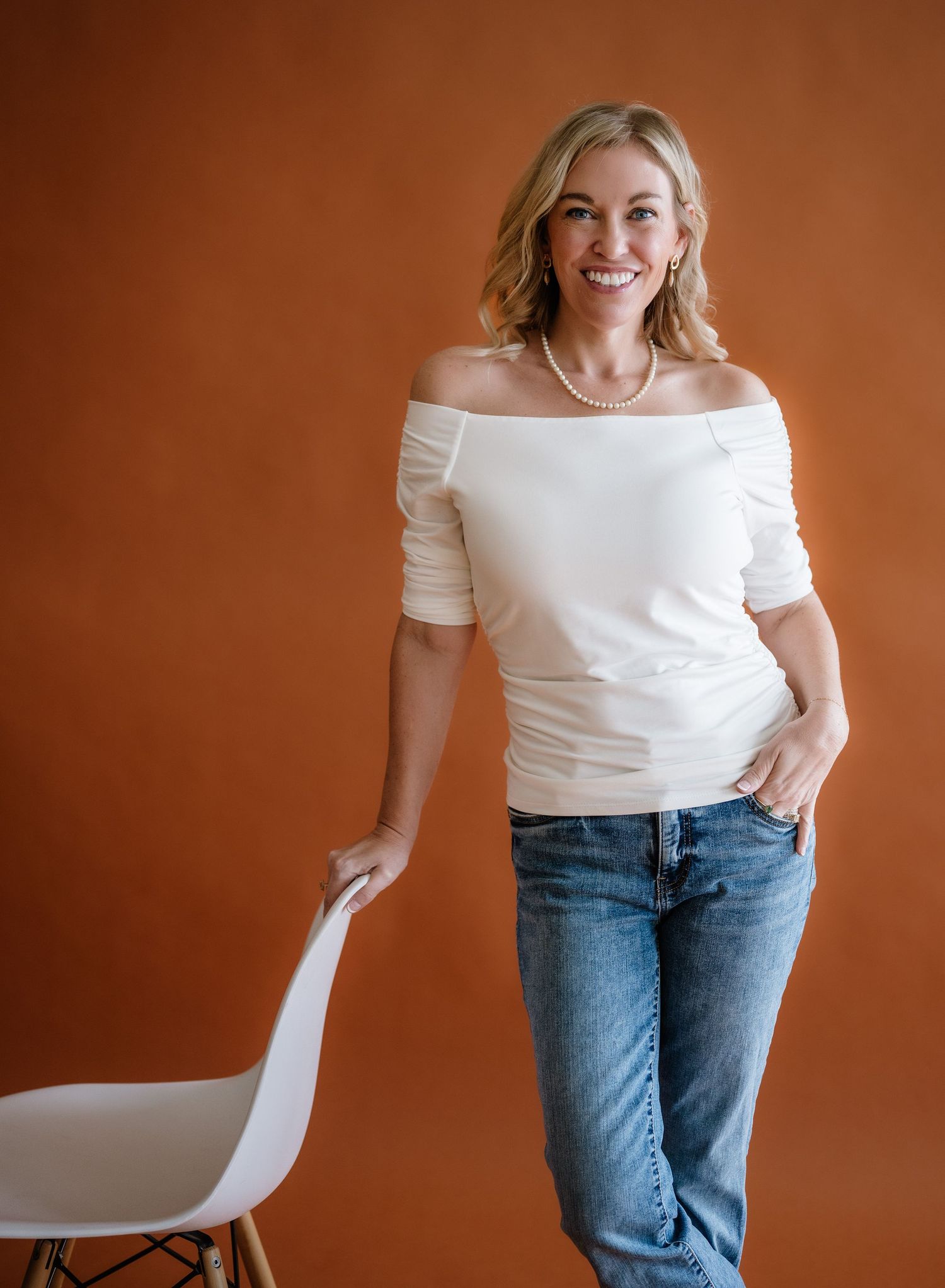 Dynamic branding photo with white off-shoulder top and jeans against warm-toned background.