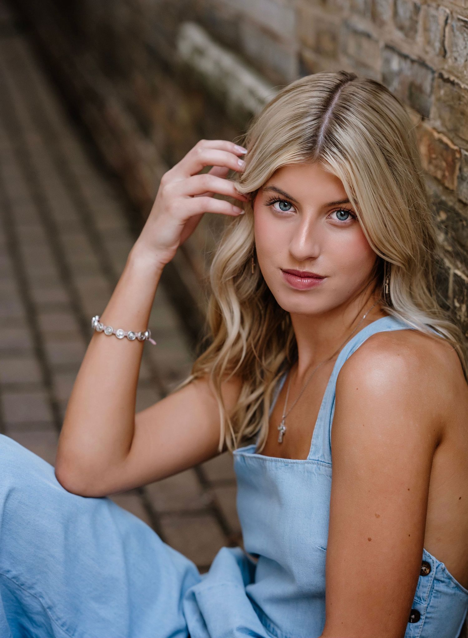 Woman in light blue top poses against stone wall during outdoor portrait session.