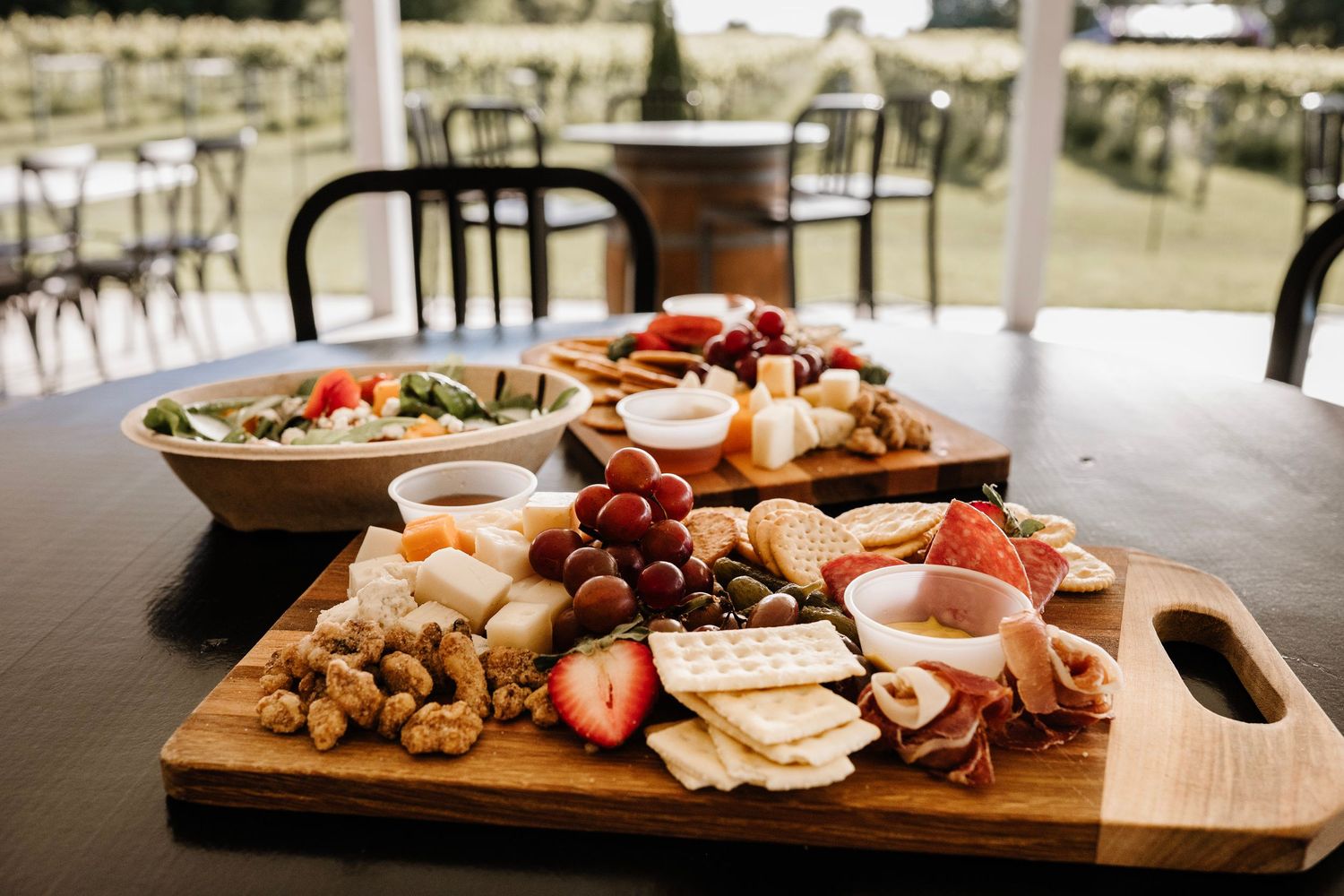 Elegant charcuterie board with cheese, crackers, grapes, strawberries, and deli meats on a wooden cutting board at an outdoor event.