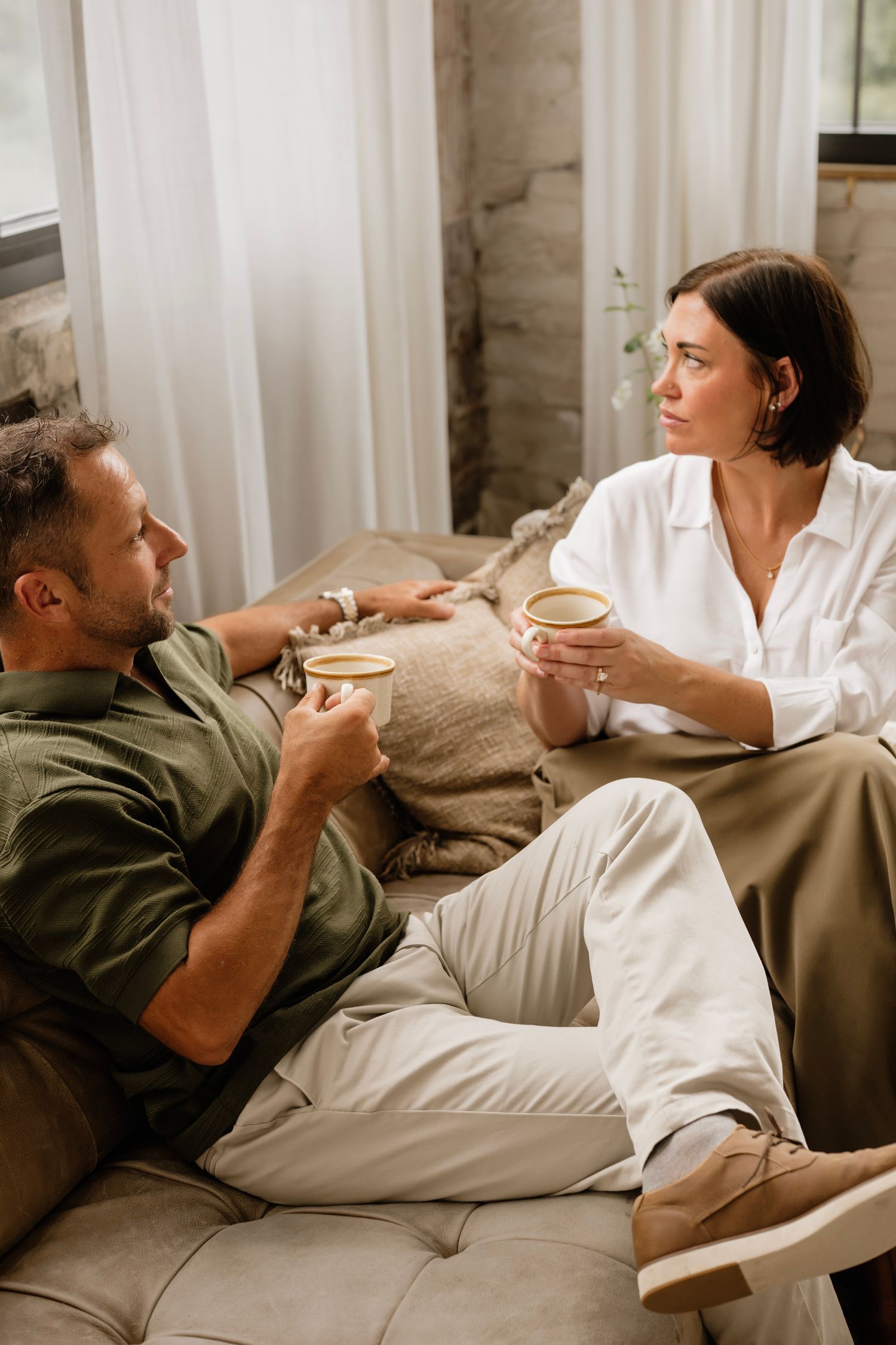 Couple relaxing on a couch, enjoying coffee together in a cozy living room setting.