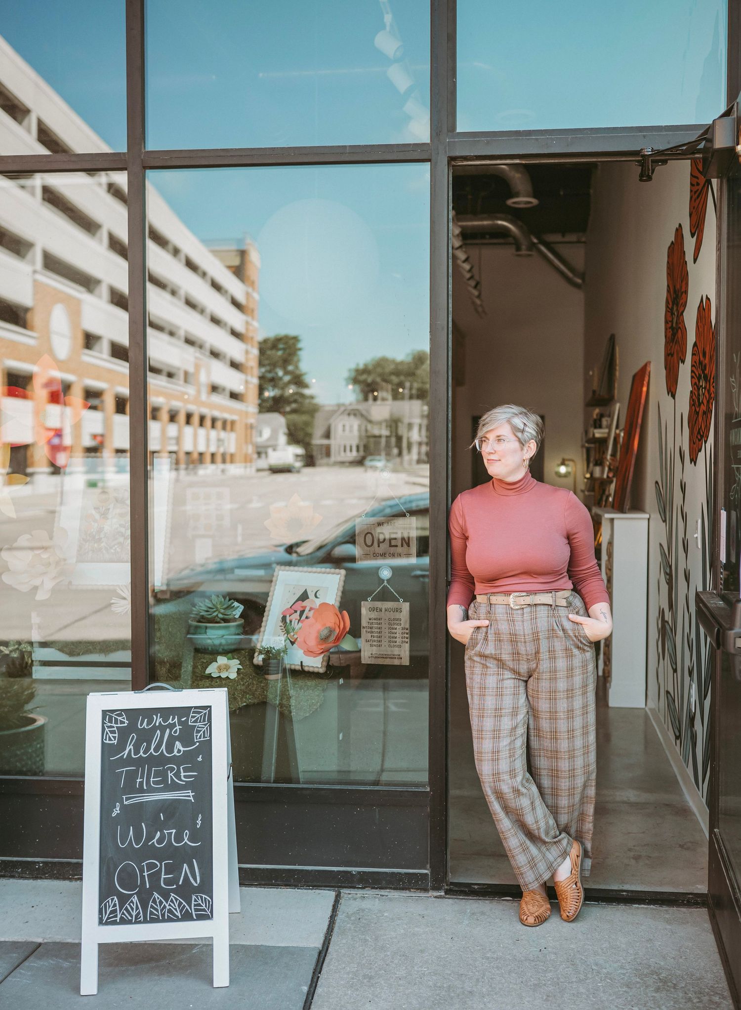 A series of storefront photos showing pink and plaid outfits with a chalkboard sign reading 'Were Open' in a retail setting.