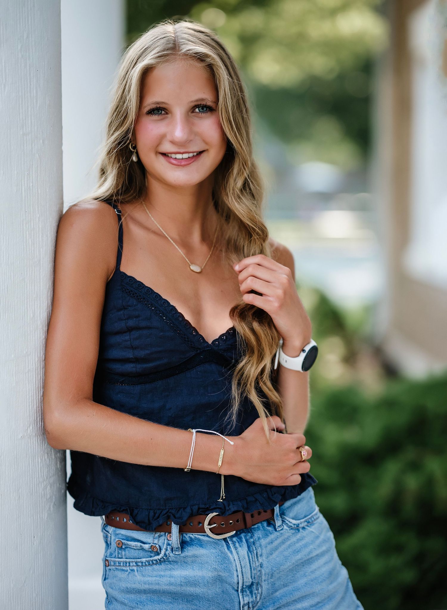 Young woman in navy blue crop top and jeans poses against white column outdoors in summer.