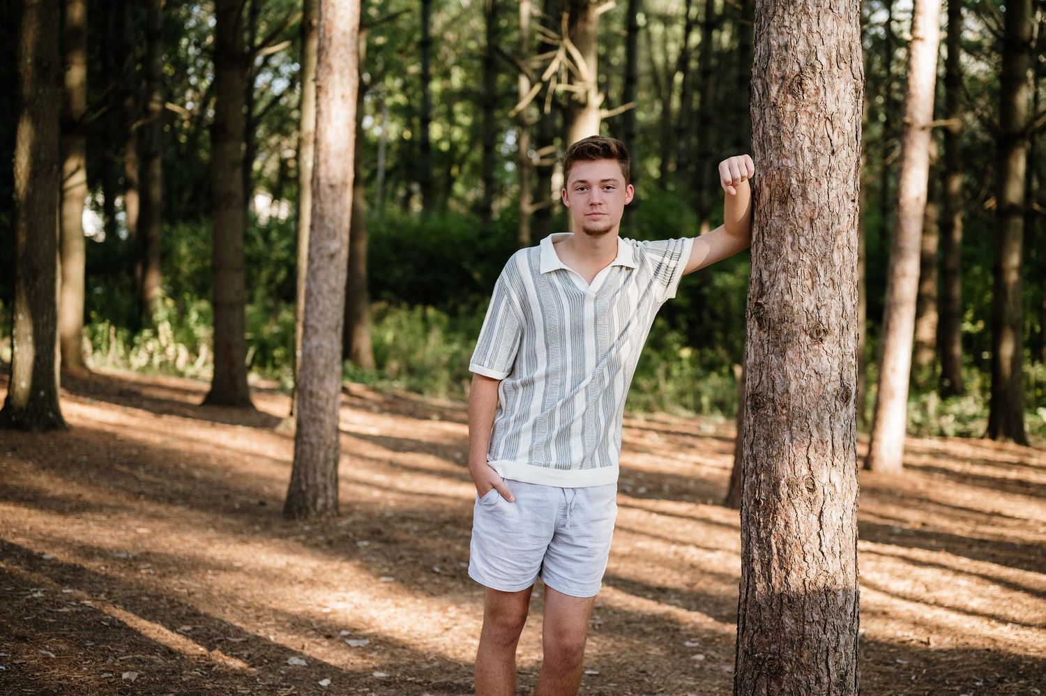 A casual summer portrait in a pine forest with striped shirt and shorts.