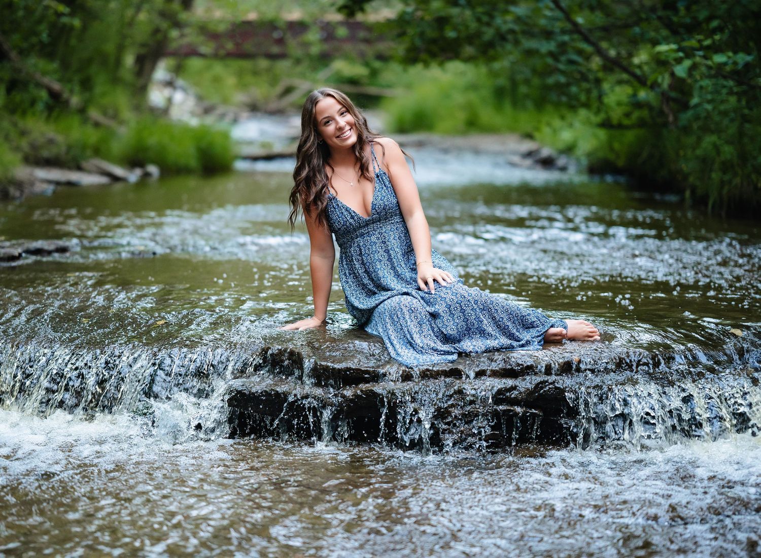 A blue dress flows gracefully as someone poses on rocks in a flowing stream.