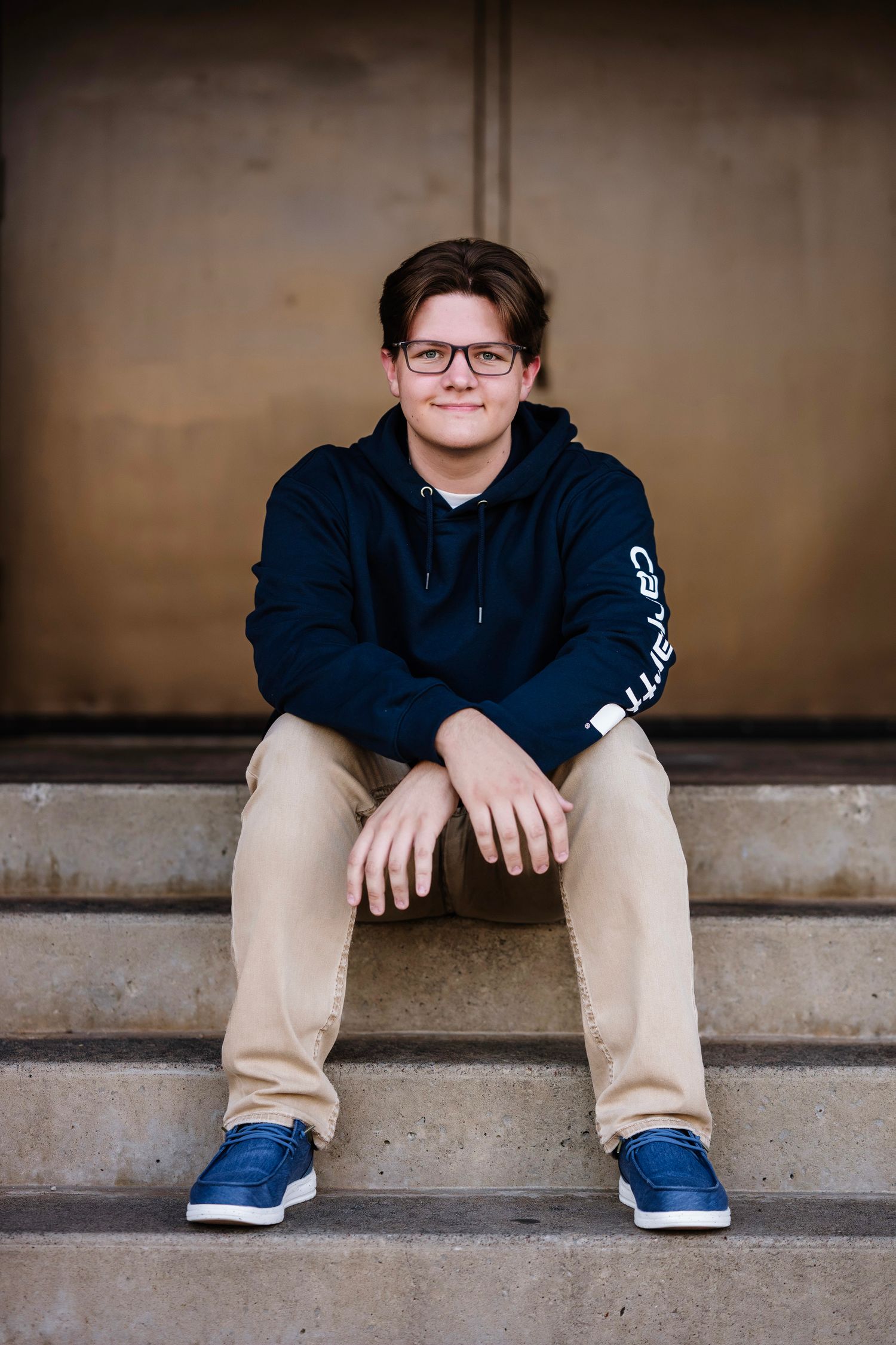 A person wearing khaki pants and blue sneakers sits on concrete steps in a casual pose.