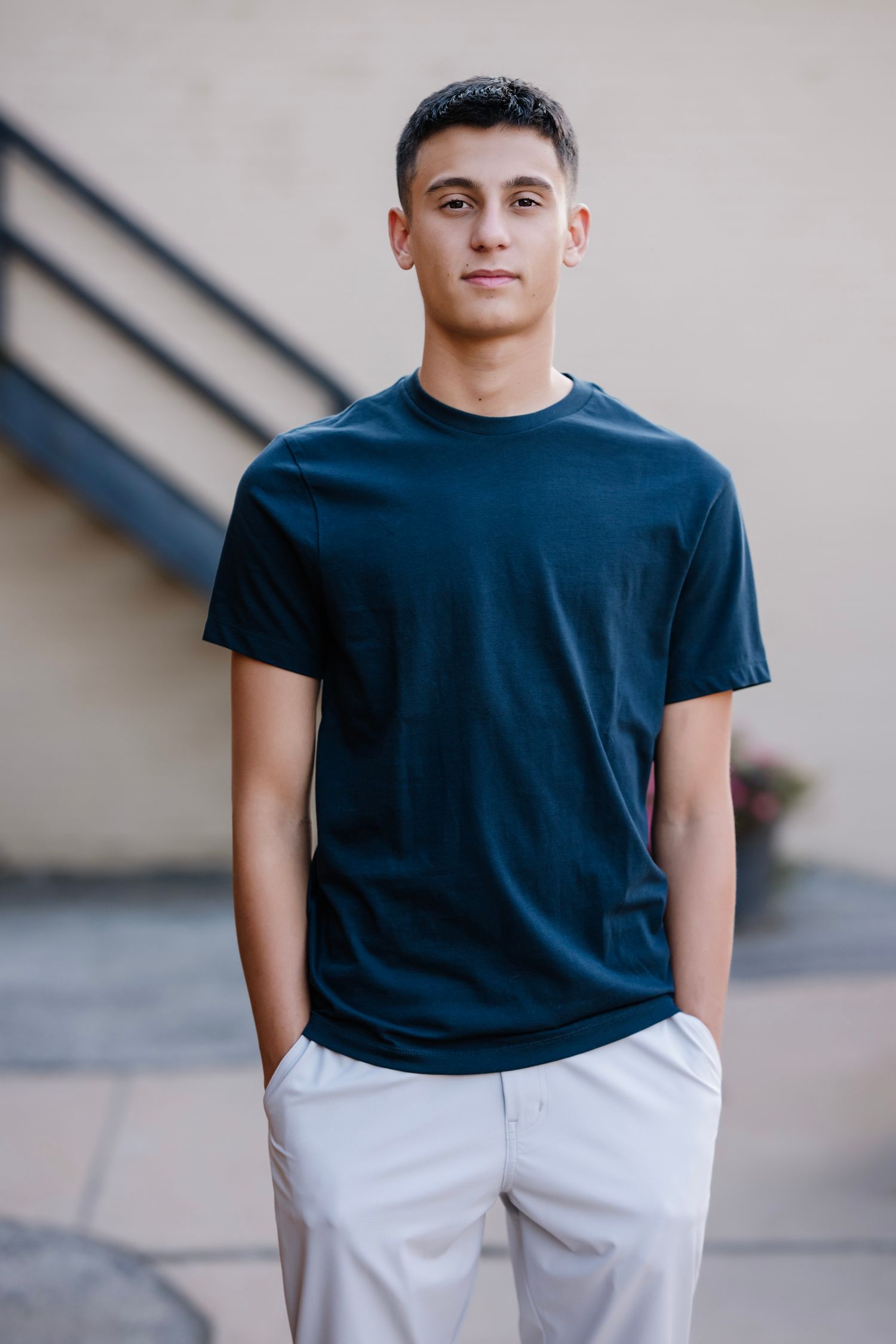 Young person wearing a navy blue t-shirt and white shorts stands confidently against a light-colored wall.