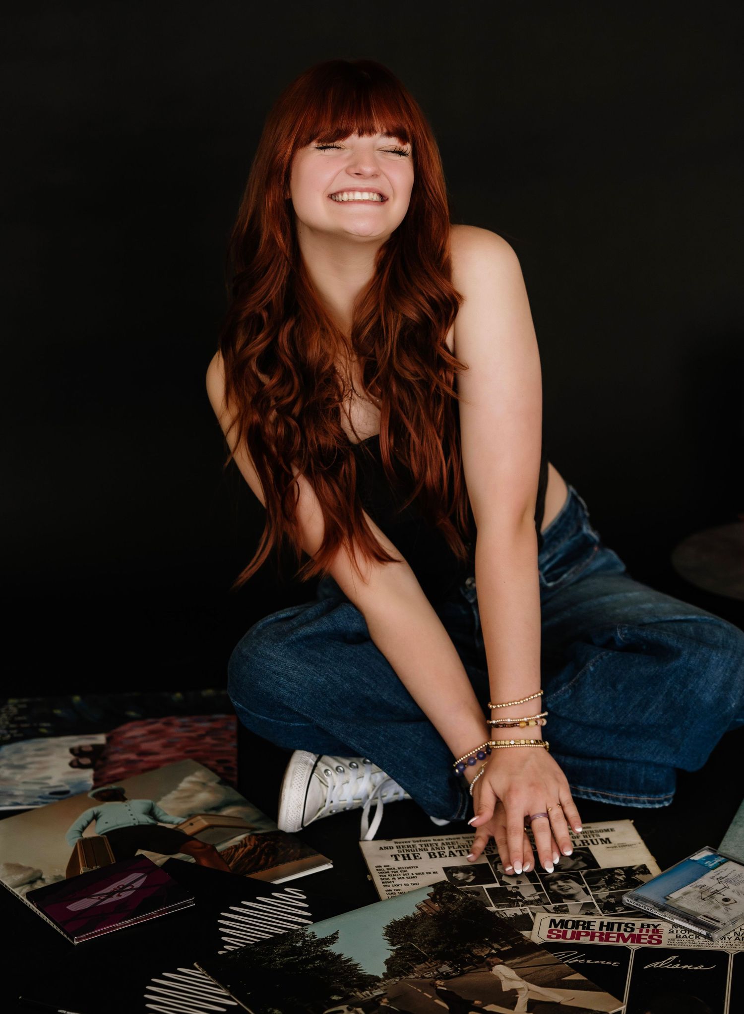 A series of five photos showing someone in denim lying on a black background with scattered vinyl records and books.