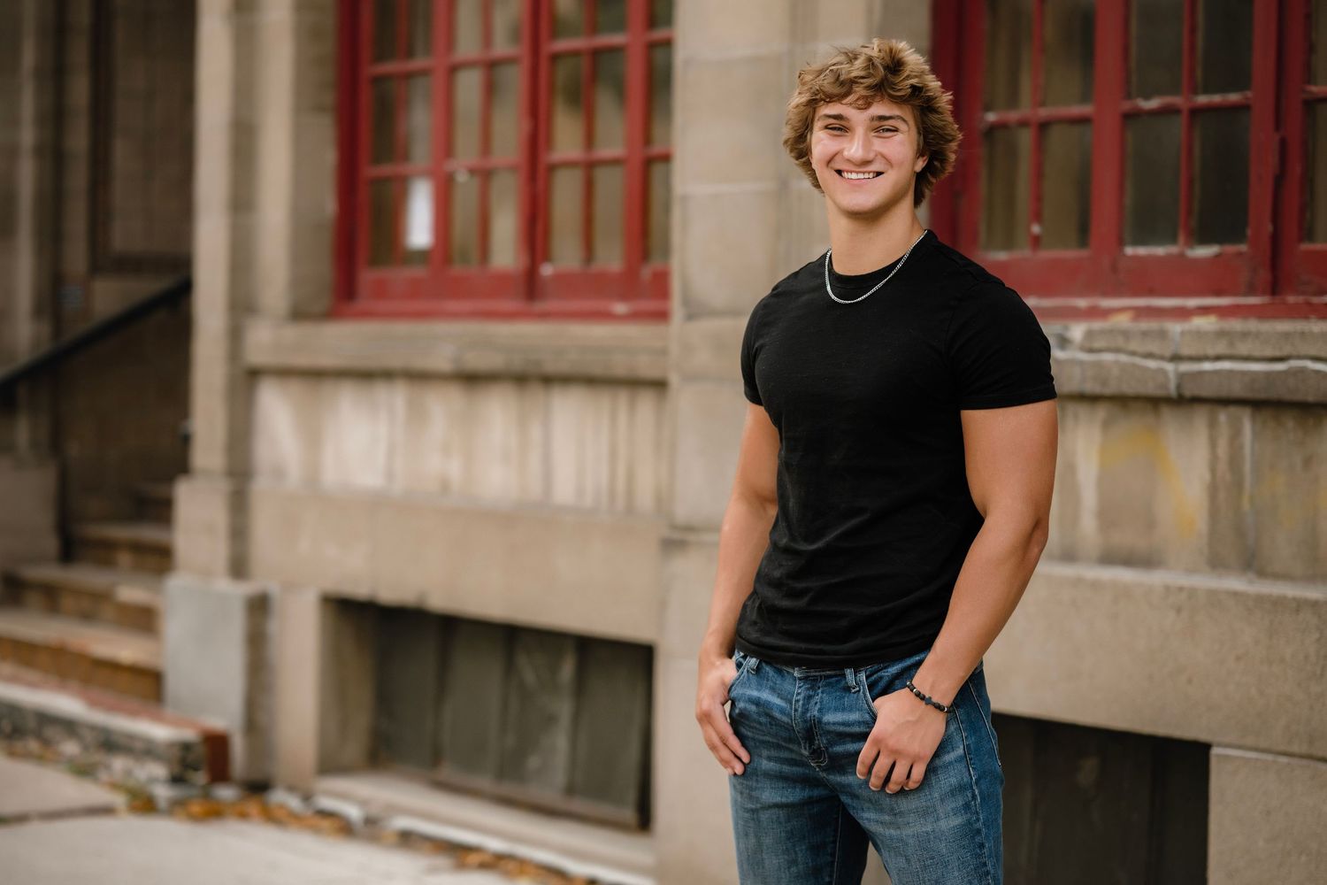 Senior portrait photos of a student in casual attire posing outdoors against a brick wall and columns.