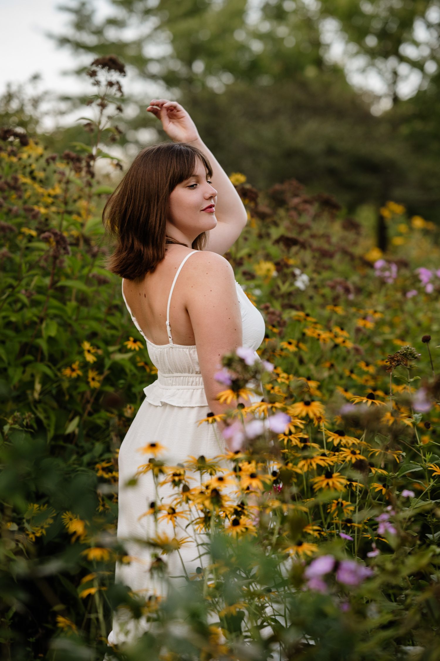 A white sundress stands out among vibrant wildflowers in a dreamy summer garden senior portrait.