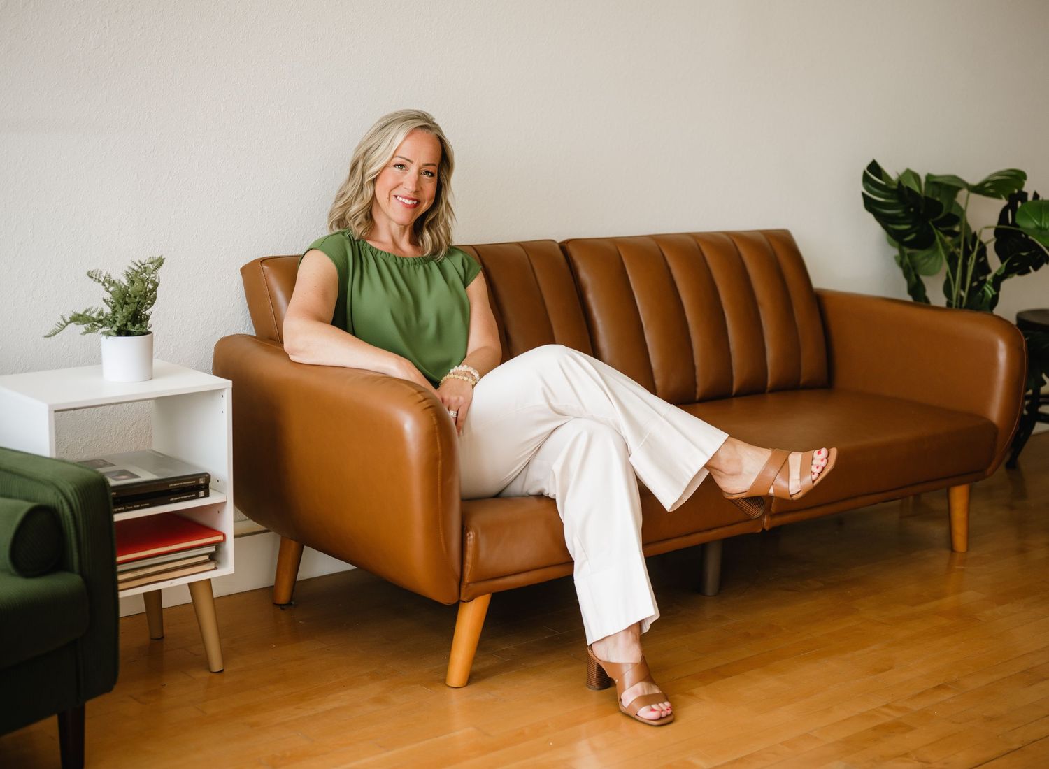 Person relaxes on a vintage brown leather couch with green plants and wood flooring in a modern living room.