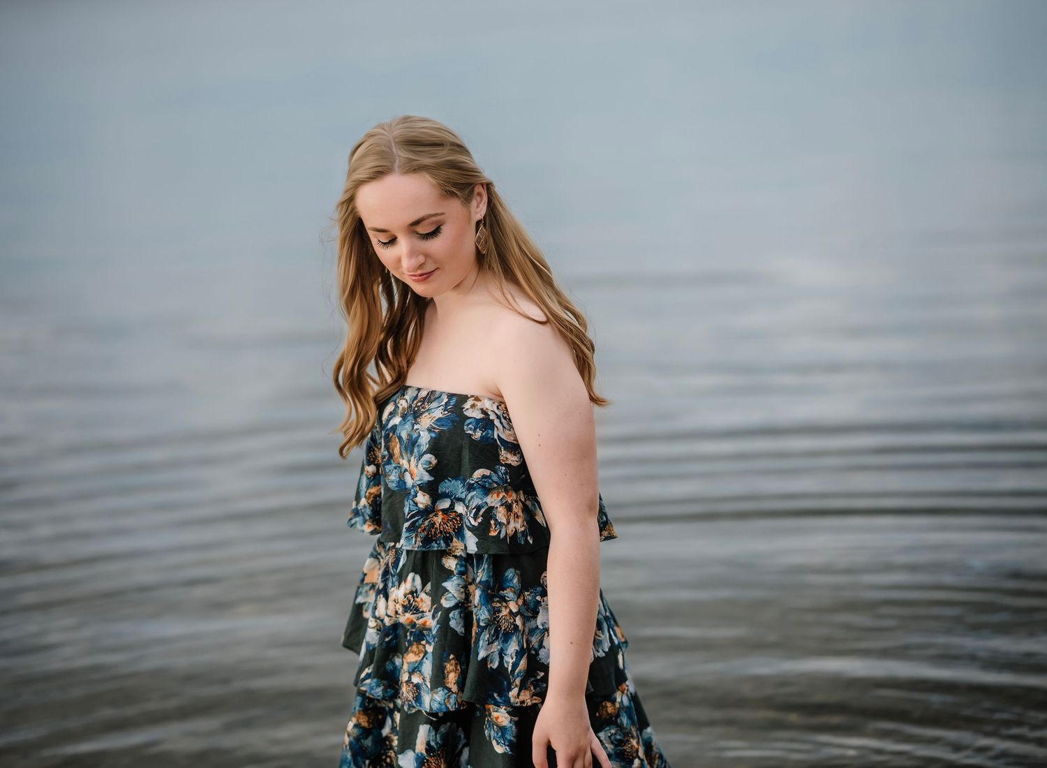Woman in floral dress walks along misty beach shoreline at sunset.