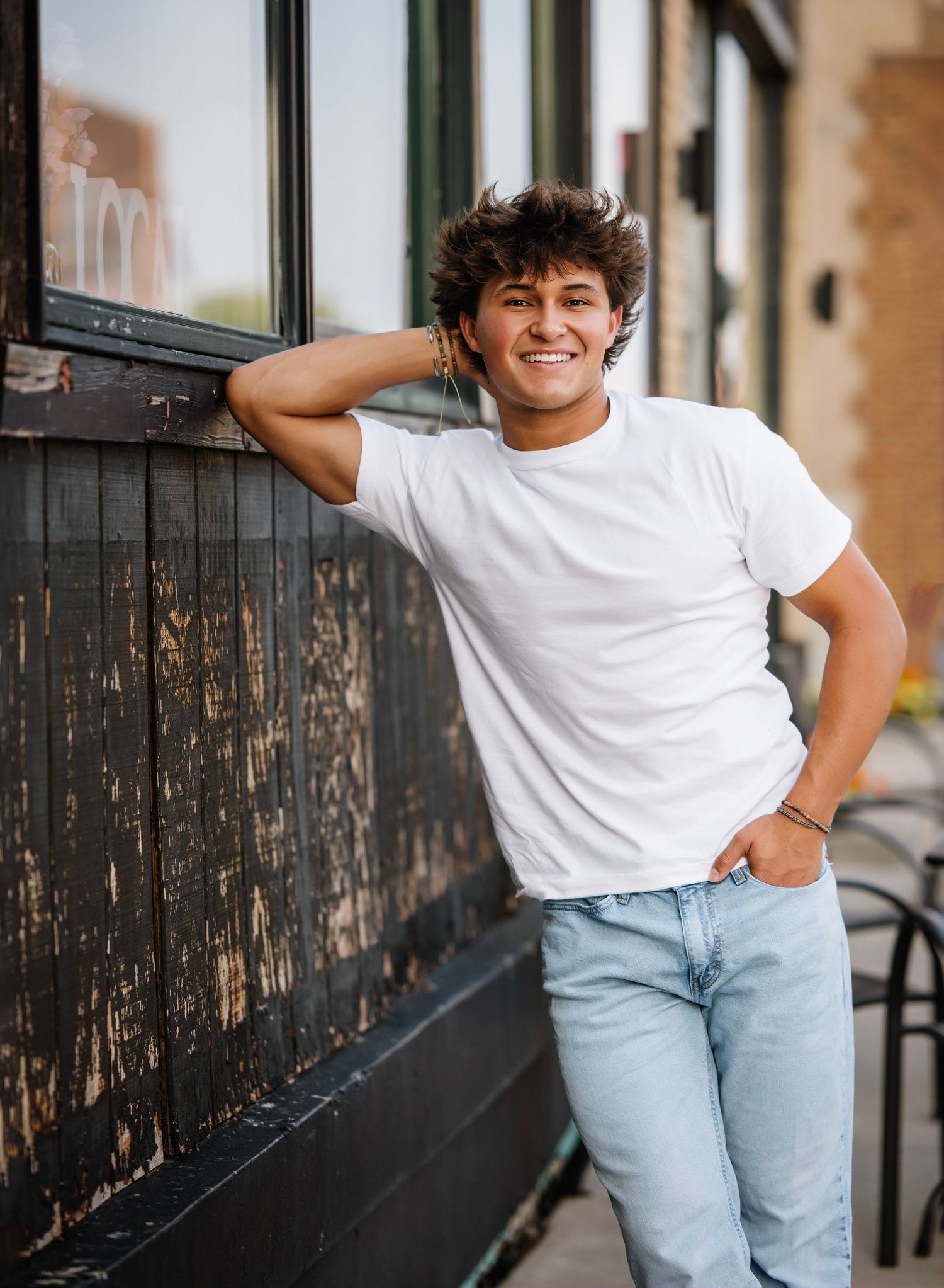 Person in white t-shirt and light jeans poses casually against dark metal railing in outdoor setting.