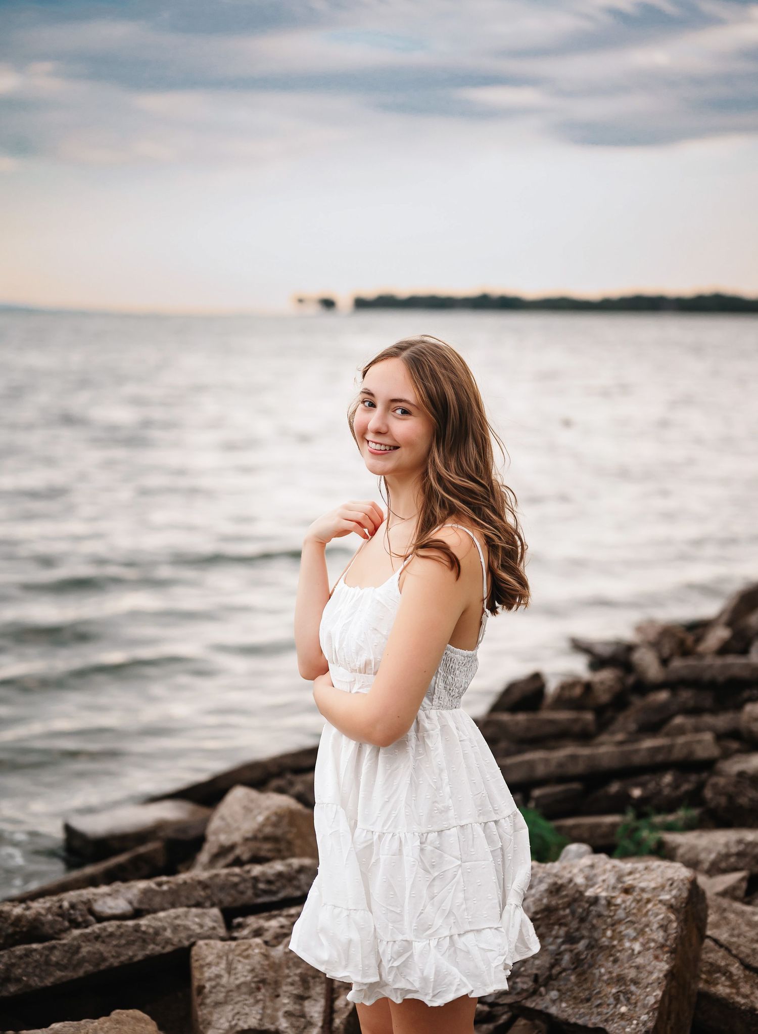 A white summer dress creates ethereal contrast against rocky shoreline and ocean waves.