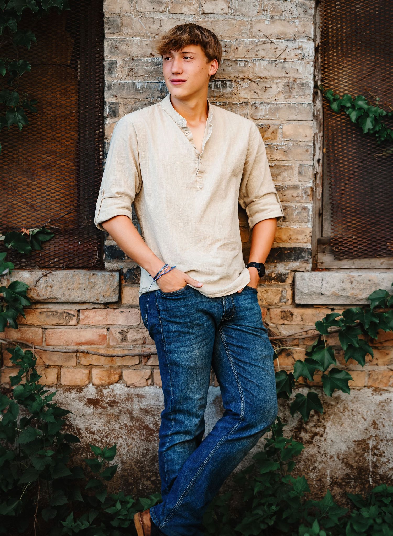 Casual senior portrait against weathered stone wall wearing beige henley and jeans.