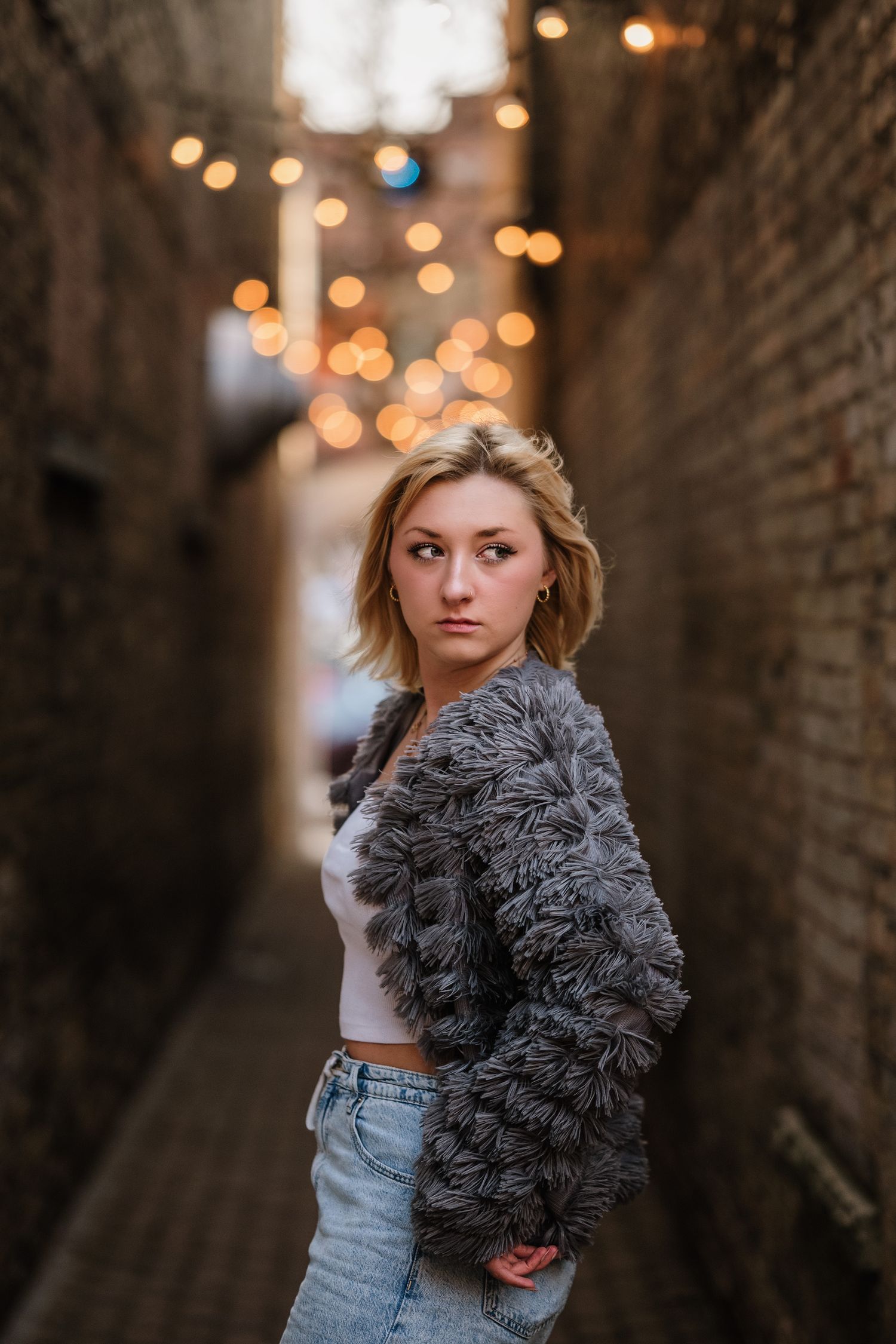 Fashion portrait in alley with string lights wearing fuzzy gray cardigan and crop top.
