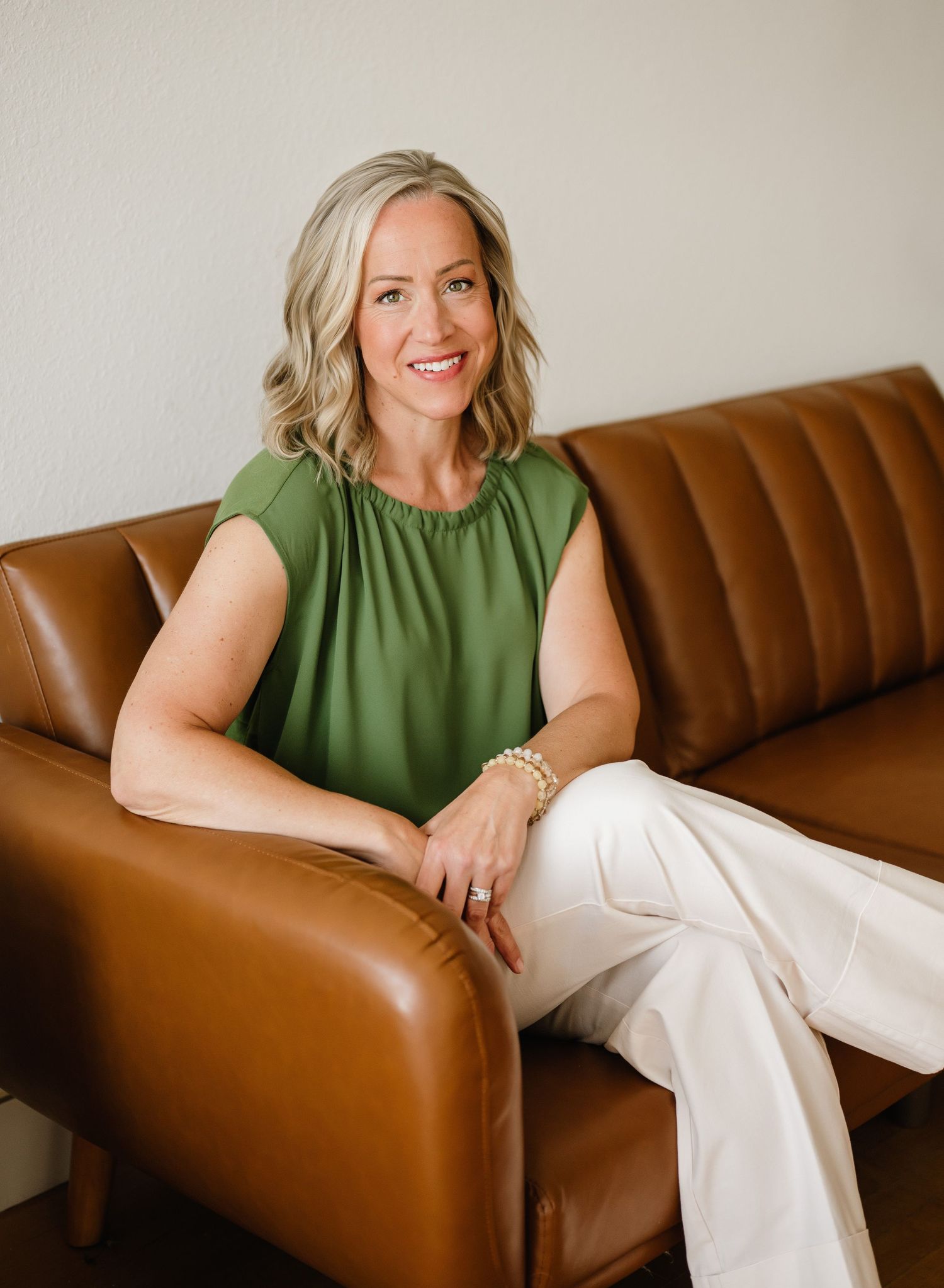 Professional lifestyle photo series of someone in a green sleeveless top and white pants relaxing on a brown leather couch.