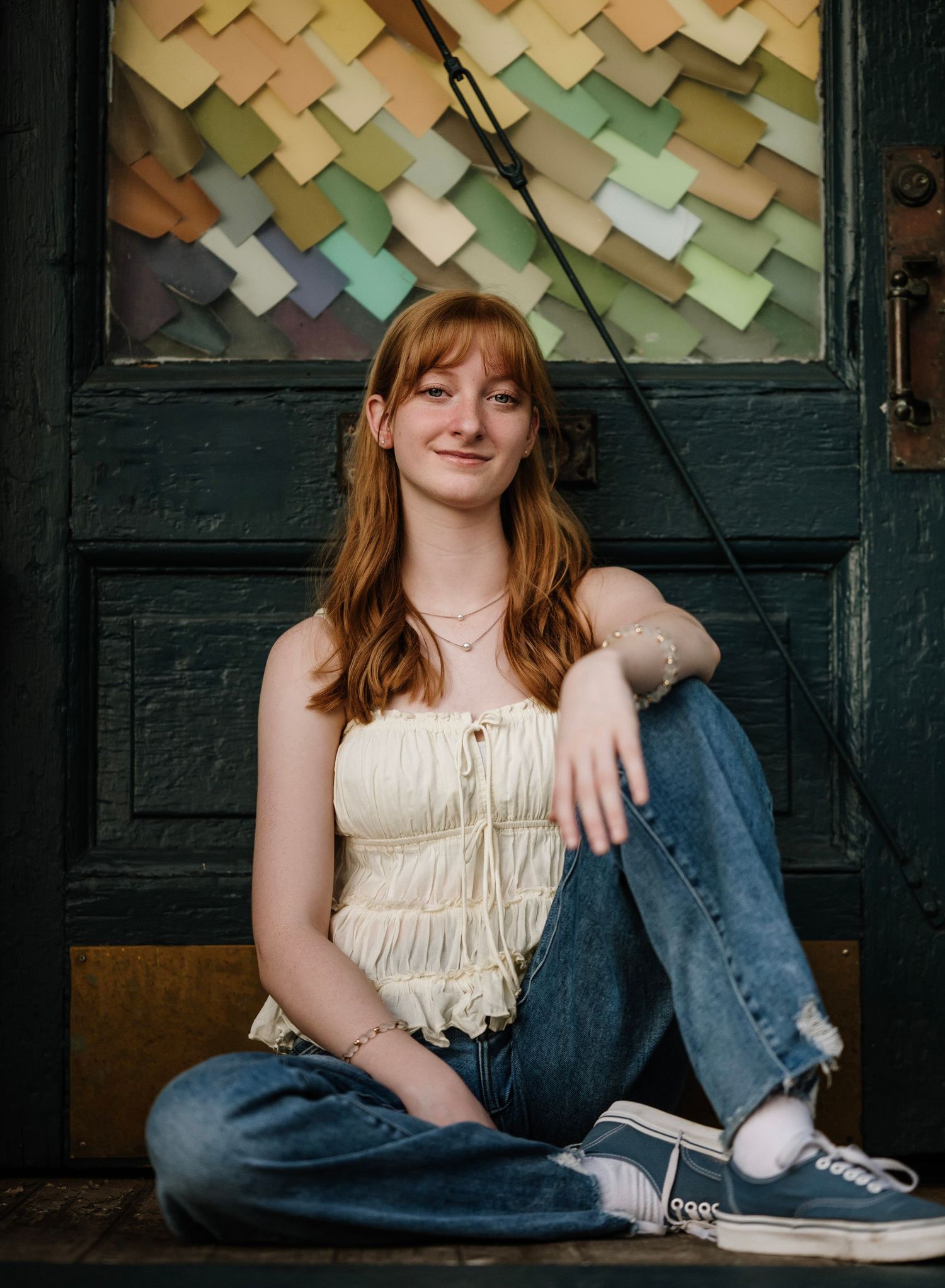A person in jeans and a cream top sits against a wall decorated with colorful overlapping paper squares.