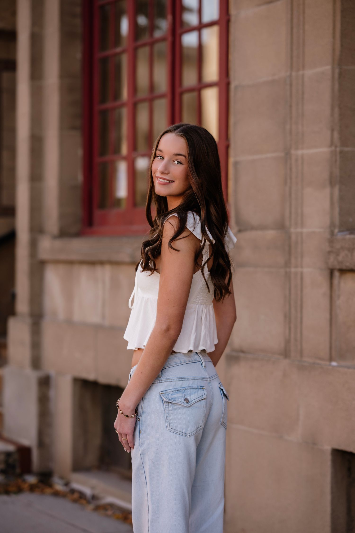 Woman in light blue overalls and white top poses against stone wall in outdoor portrait session.